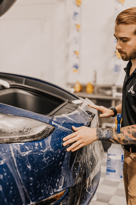 A man is applying a protective film to the front of a car.