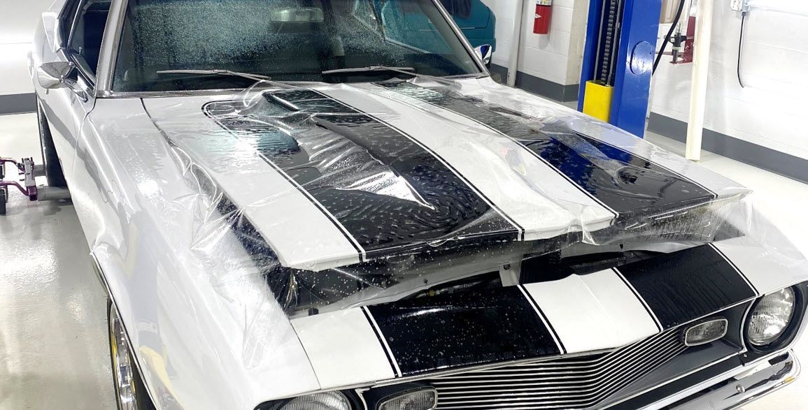 A white car with black stripes is wrapped in plastic in a garage.