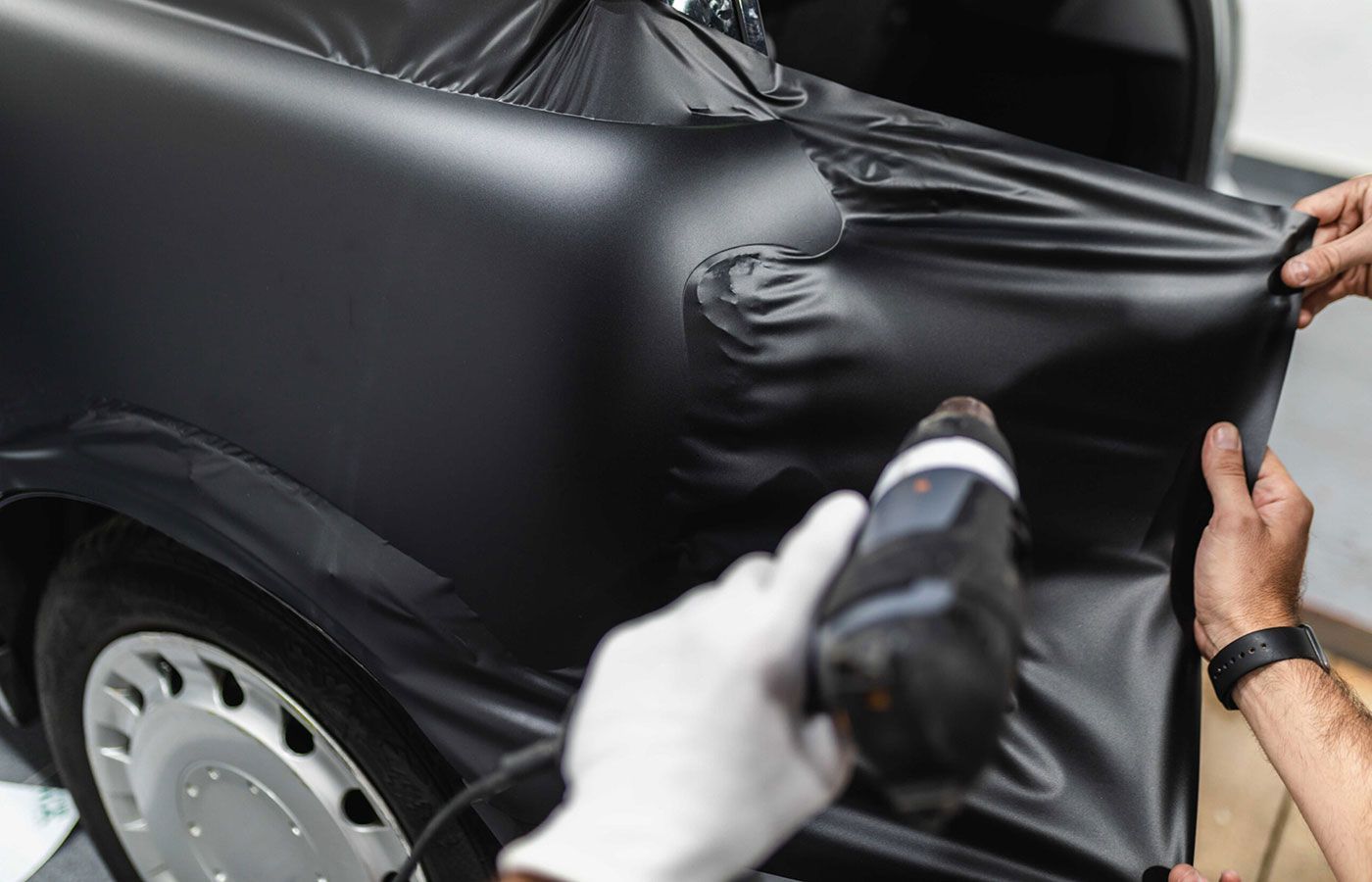 Close-up of a matte black vinyl being stretched and heated onto a car panel using a heat gun
