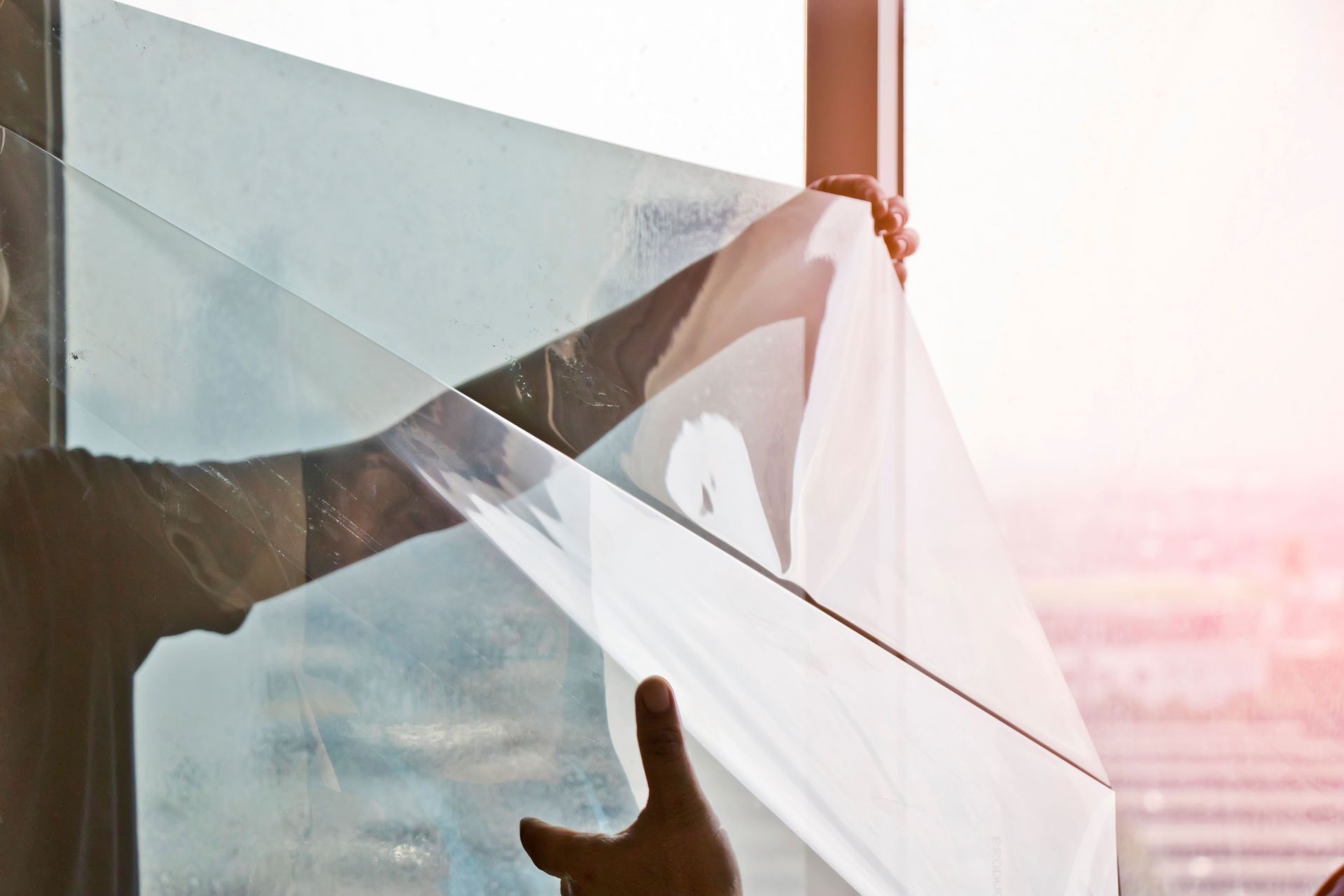 Person installing window film on a high-rise window, with a cityscape visible outside.
