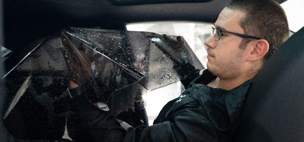 A man is sitting in a car holding an umbrella.