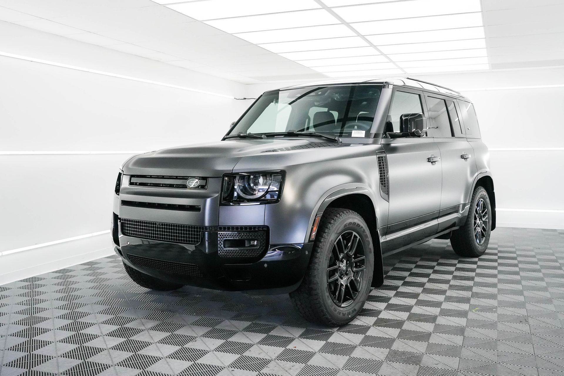 A gray land rover defender is parked on a checkered floor in a showroom.