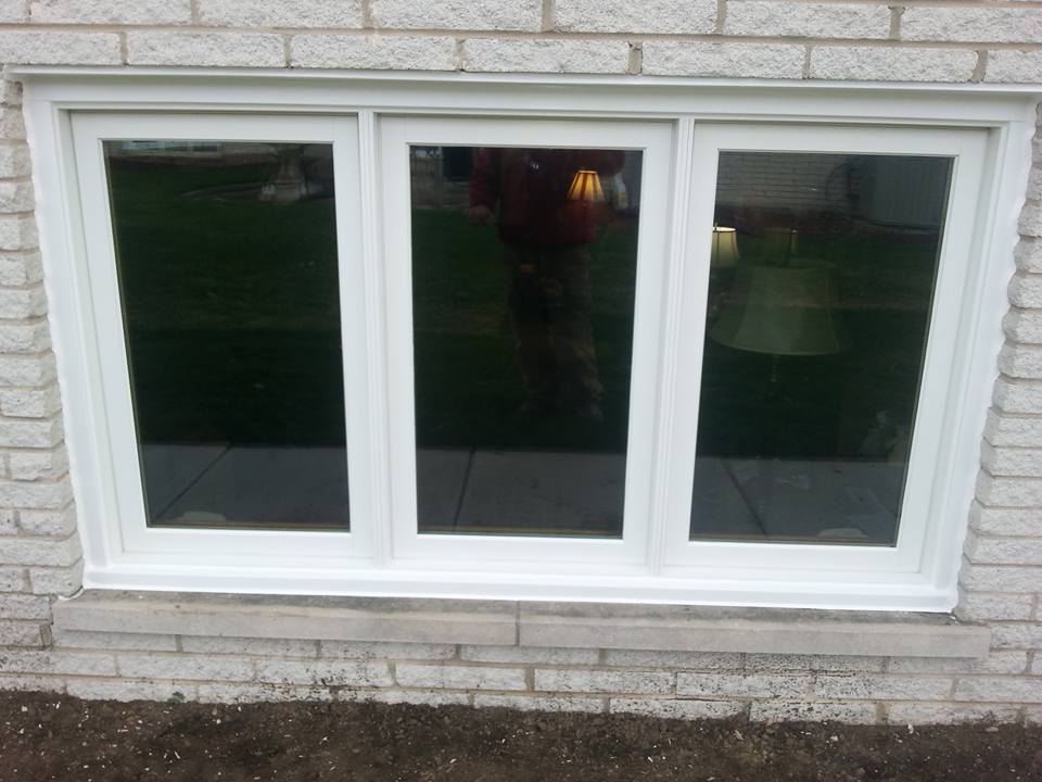 A white window with three windows on a brick wall.