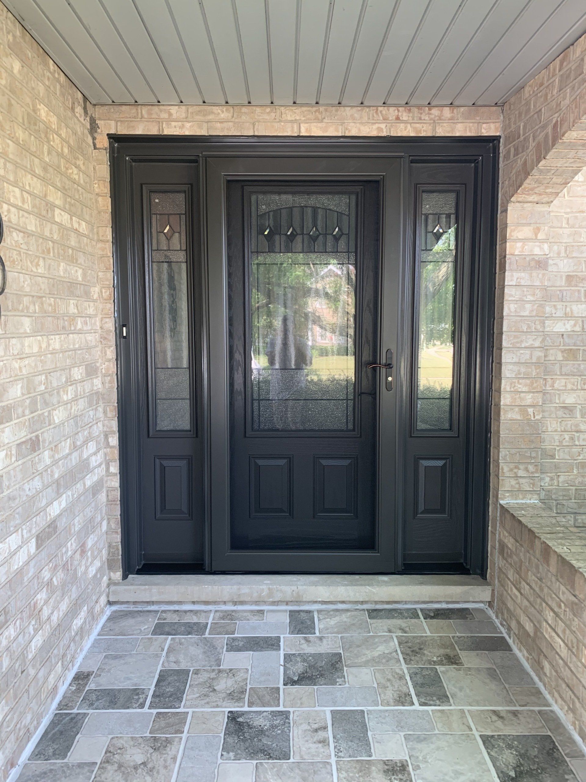 The front door of a brick house with a black door and a tiled floor.