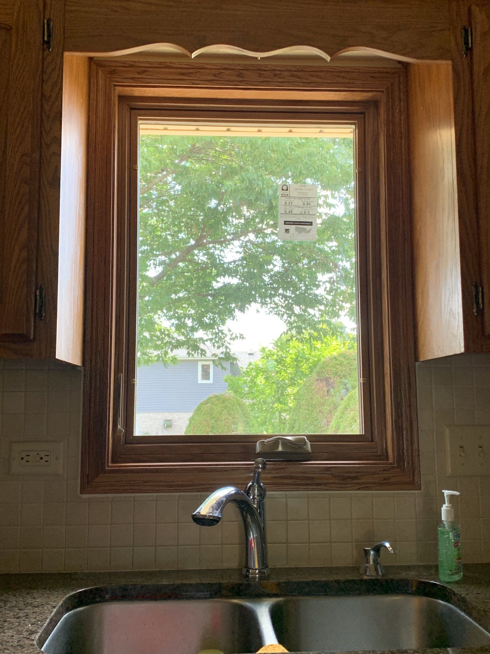 A kitchen sink under a window with a view of trees
