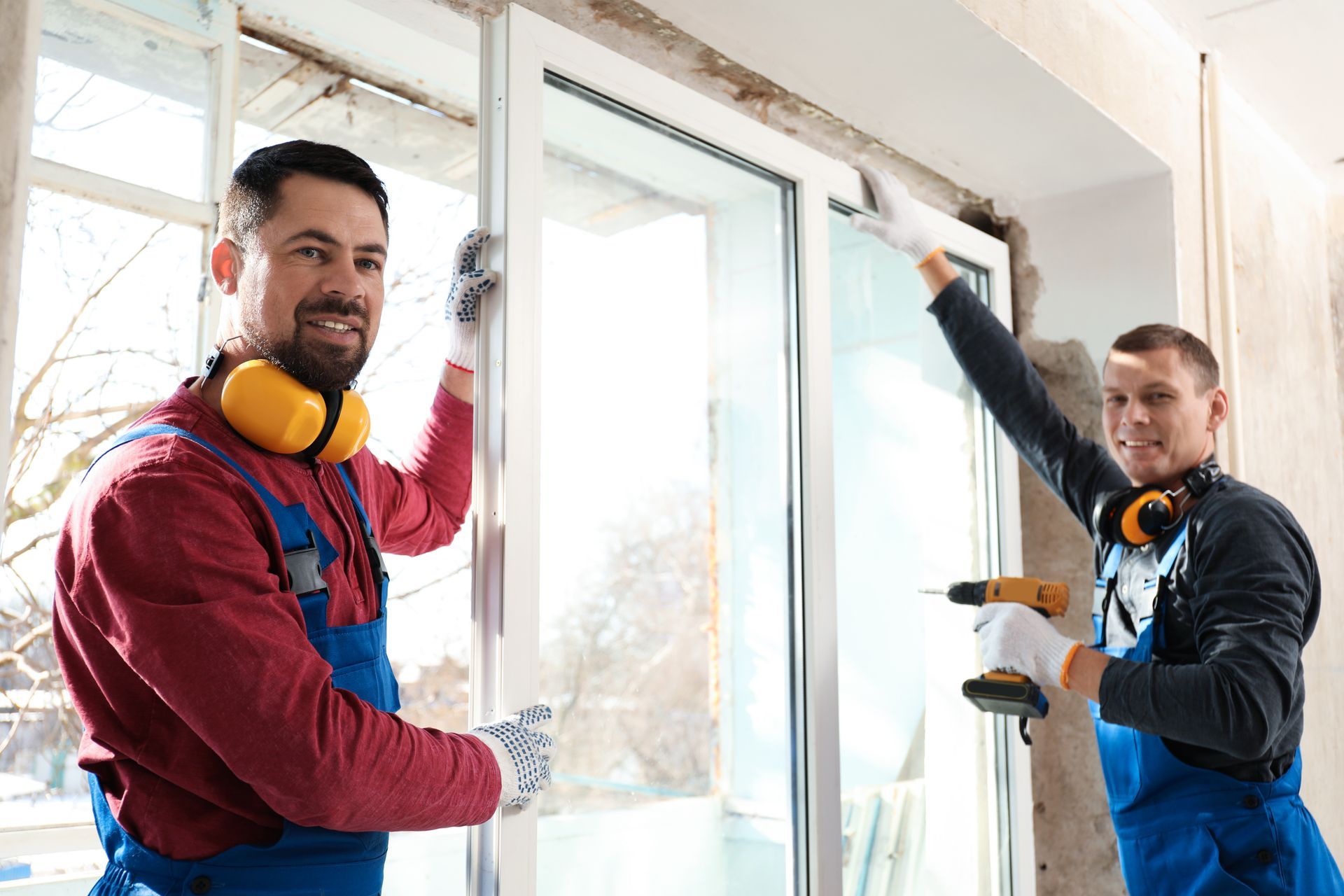 Two workers are using an electric screwdriver for a window installation indoors. Two workers are using an electric screwdriver for a window installation indoors.