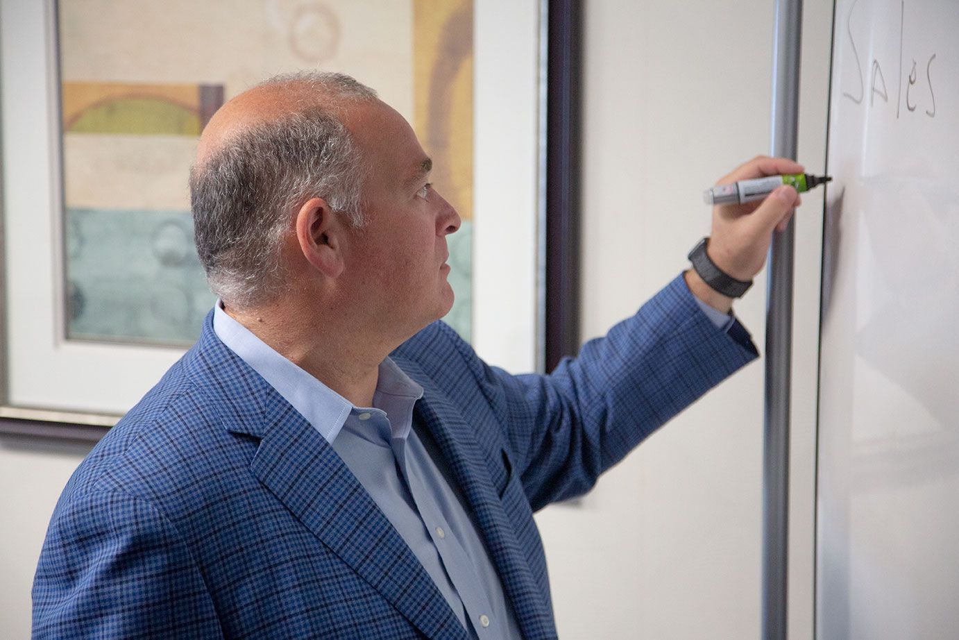 a man in a suit is writing on a white board with a green marker
