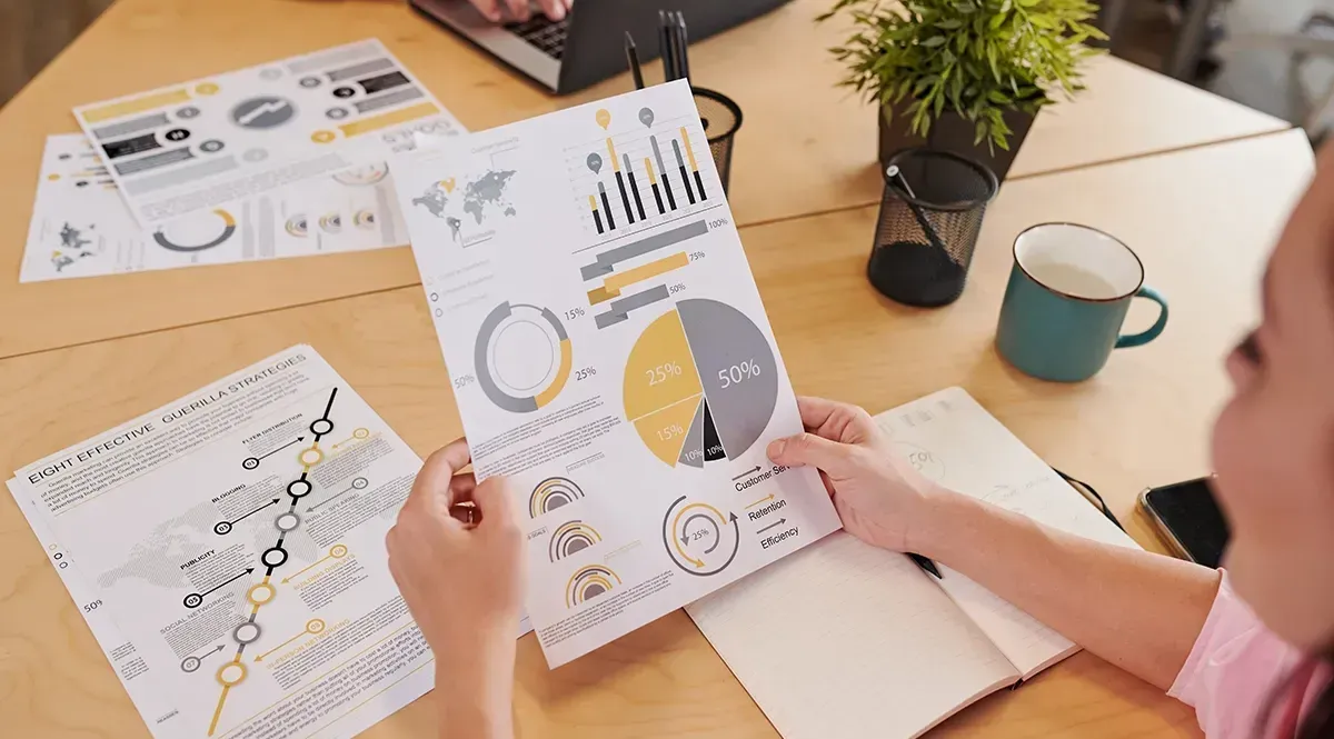 A woman is sitting at a table holding a piece of paper with a pie chart on it.