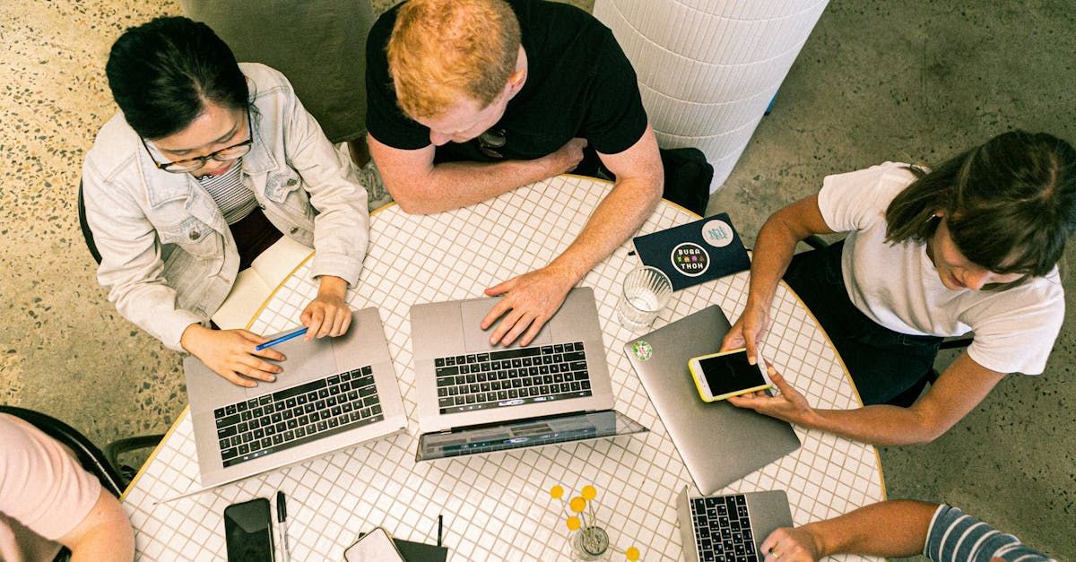 A group of people are sitting around a table with laptops.