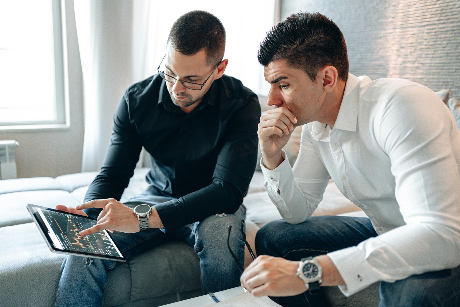 Two men are sitting on a couch looking at a laptop.