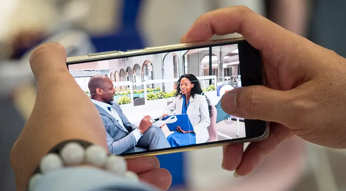 A person is holding a cell phone in their hands and taking a picture of a man and woman.