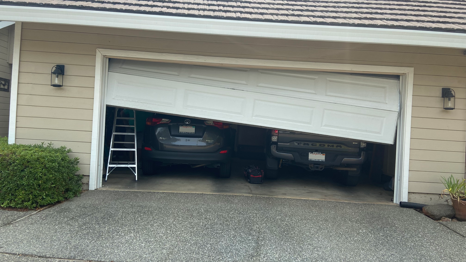 A crashed garage door hanging at an angle trapping two cars inside. 