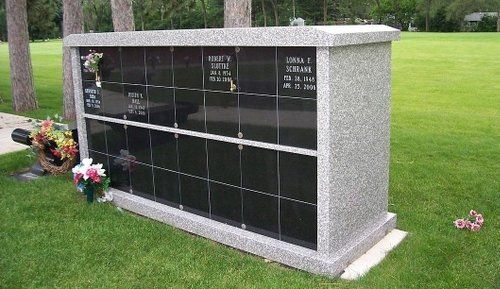A granite columbarium with black niches in a grassy cemetery.