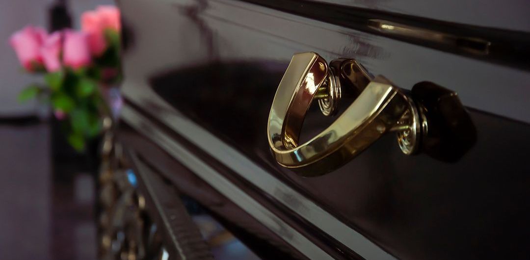 Close-up of a gold handle on a dark wooden drawer. Pink flowers are slightly visible in the background.