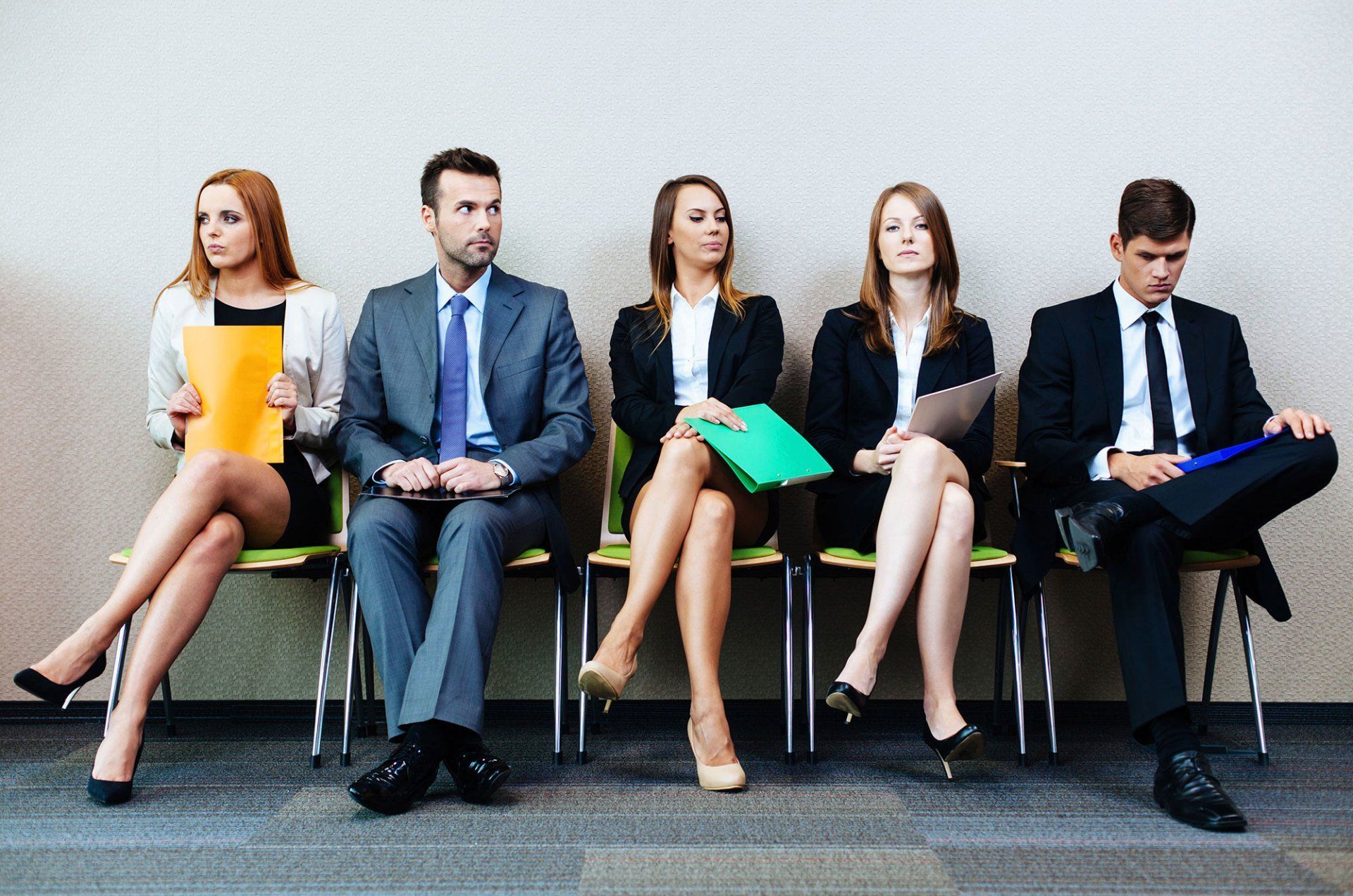 People in business attire seated, waiting; one looks bored, others are attentive.