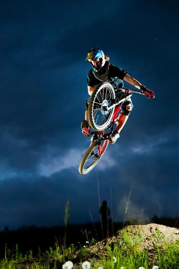 Mountain biker airborne over a dirt jump at night under a deep blue sky