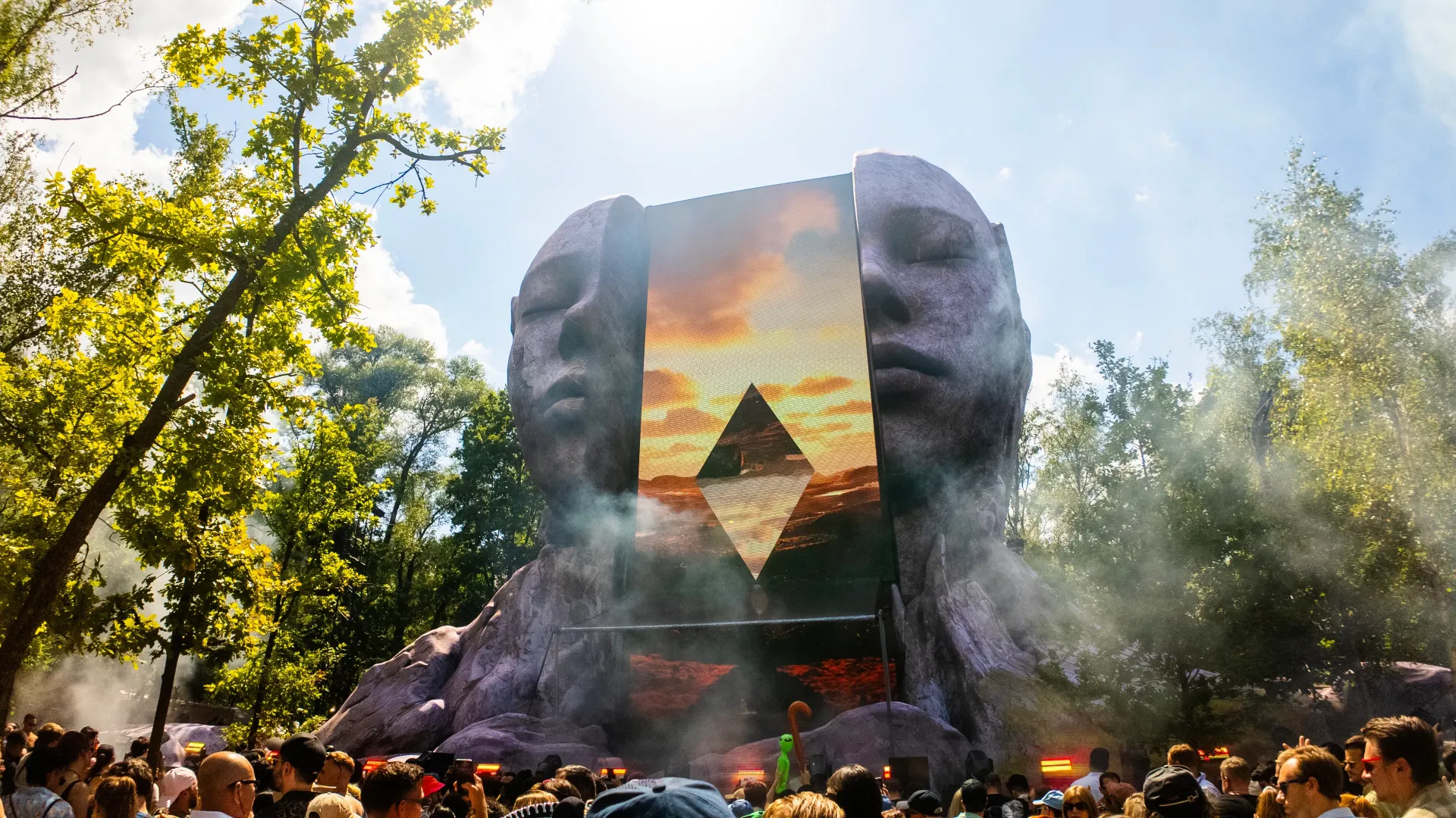 Crowd watching a giant stage with a glowing geometric display in a forest clearing