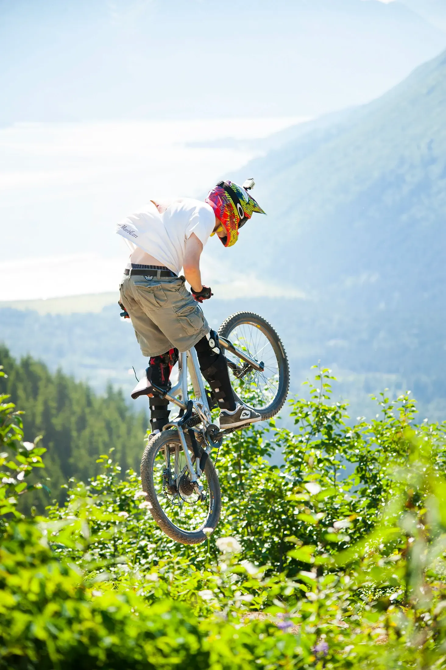 Mountain biker mid-jump on a trail with a forested valley and mountains in the background