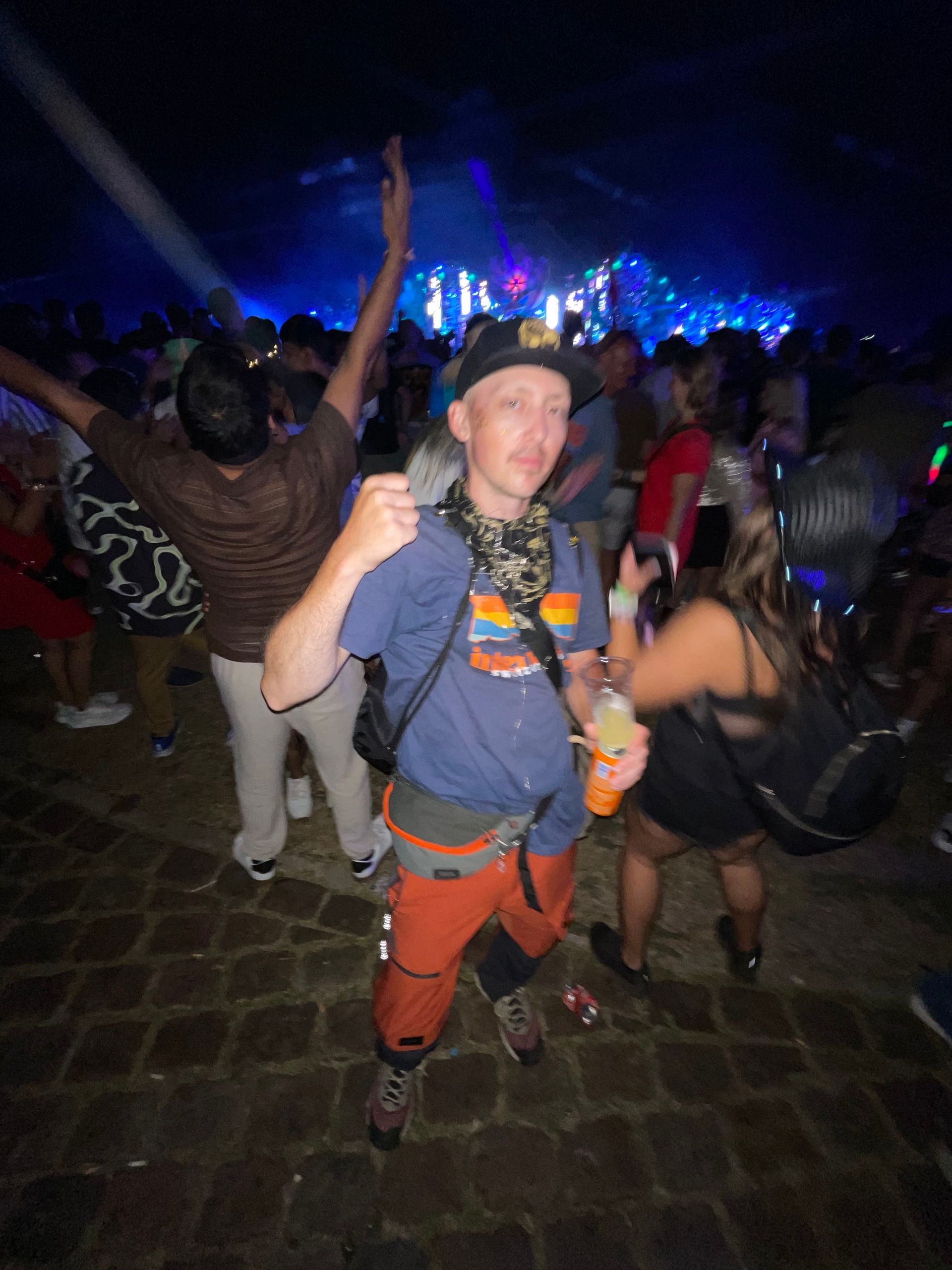 Person in a blue shirt and orange pants giving a thumbs-up in a crowded nighttime concert crowd