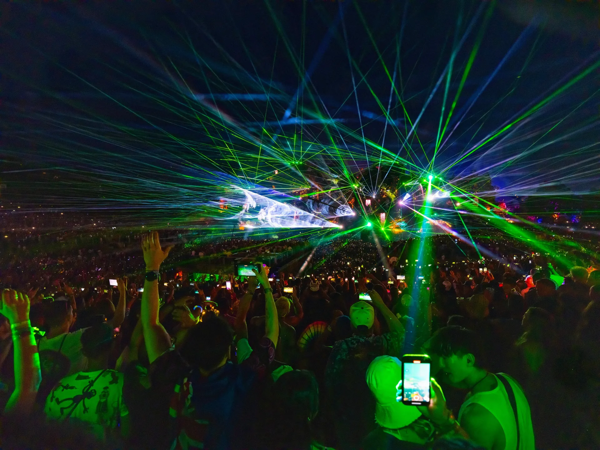 Crowd at a nighttime concert with green laser lights and a person holding up a phone