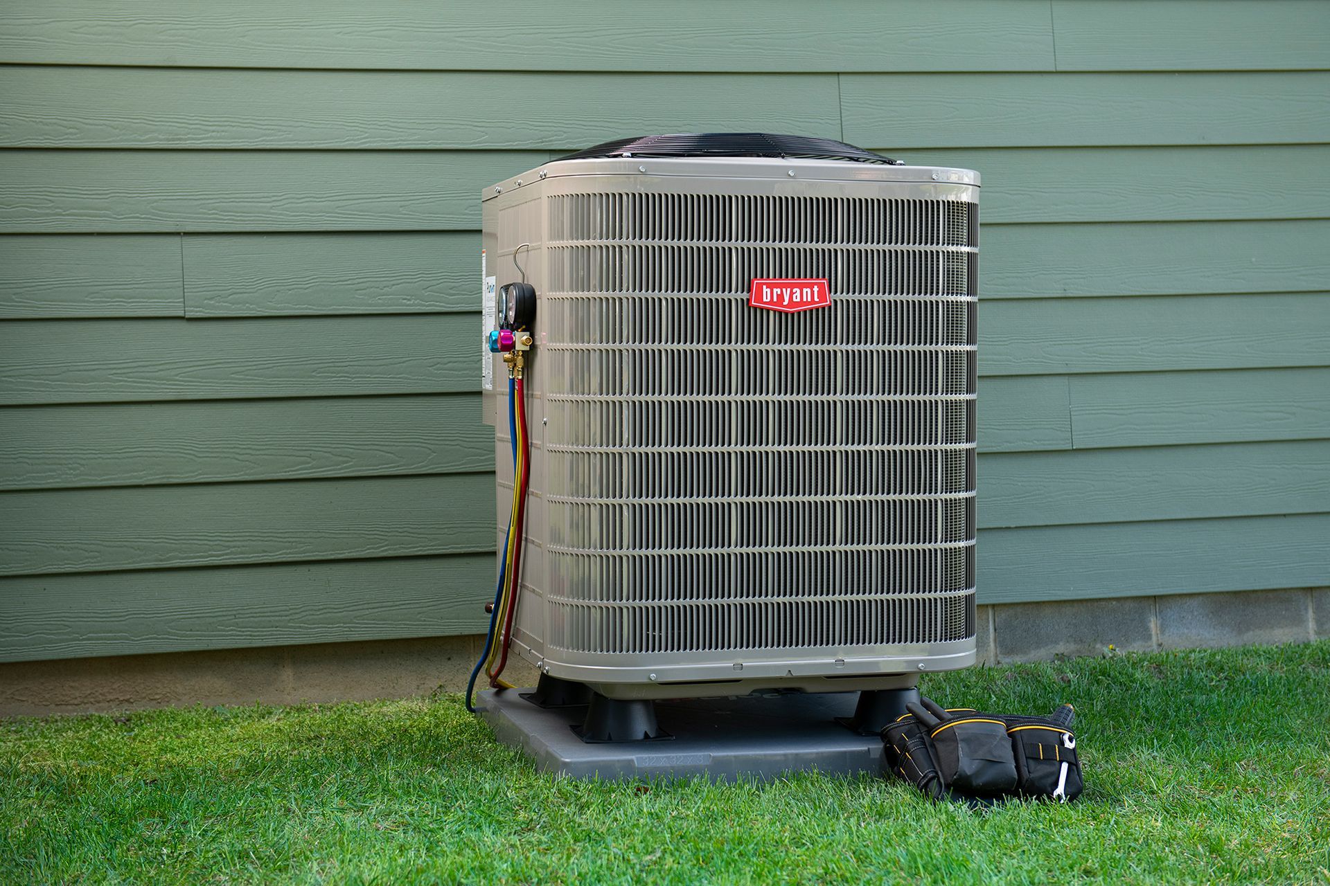 Air conditioner unit sitting on a concrete pad in a grassy yard, next to a green wall.