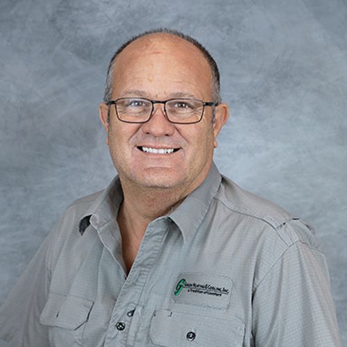 Man wearing glasses and gray shirt smiles at the camera.