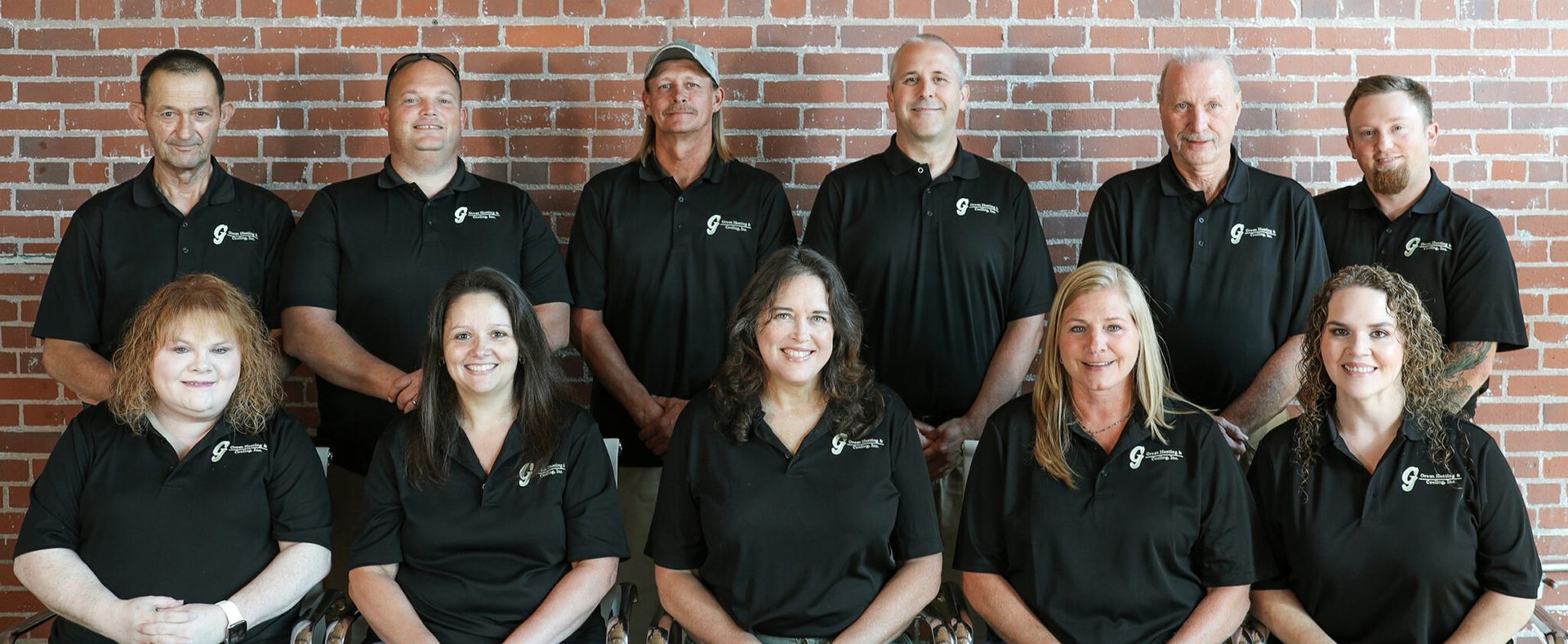 Group of people in black shirts posing in front of a brick wall.