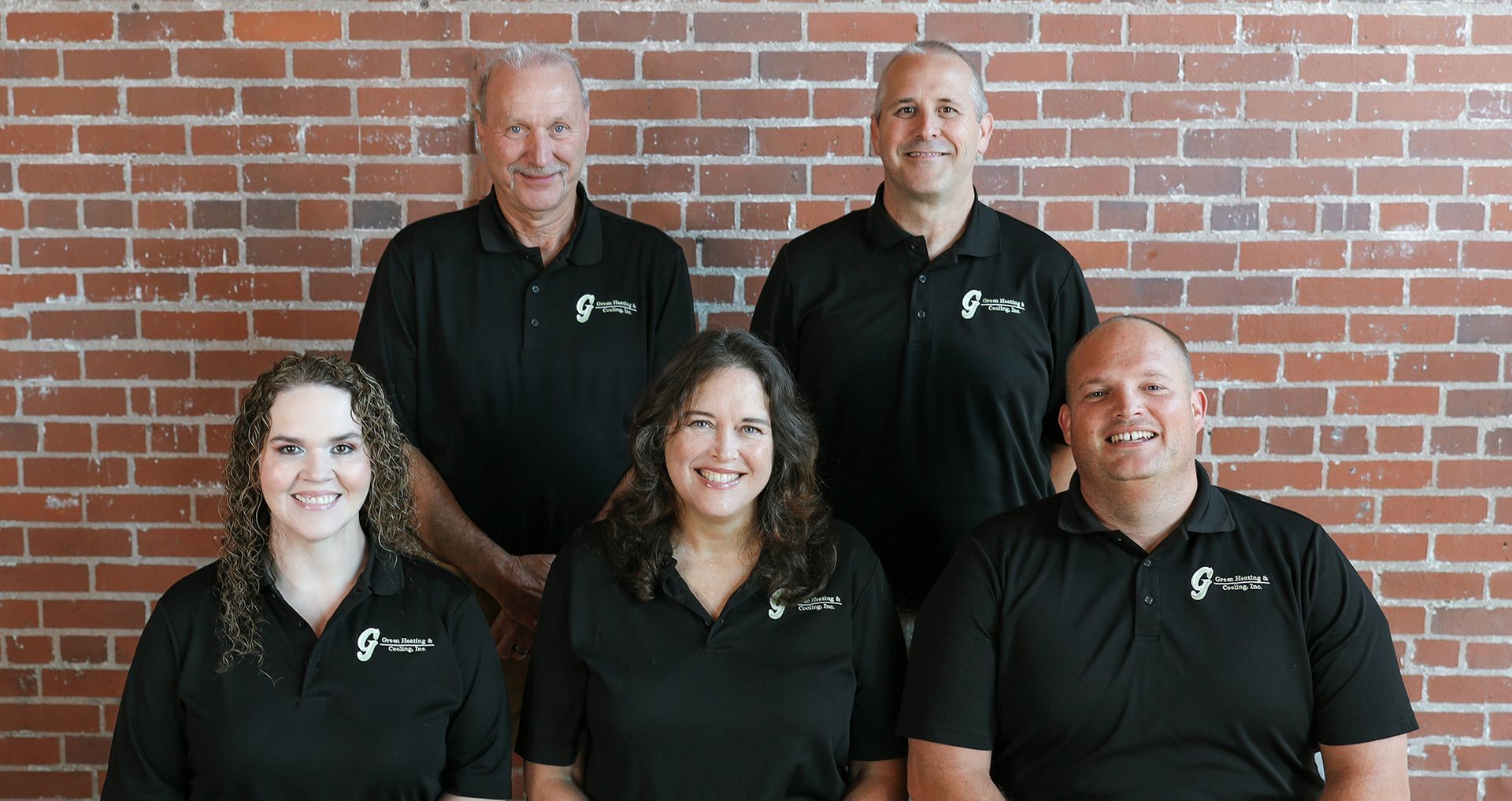Group of five people in black shirts posing in front of a brick wall.