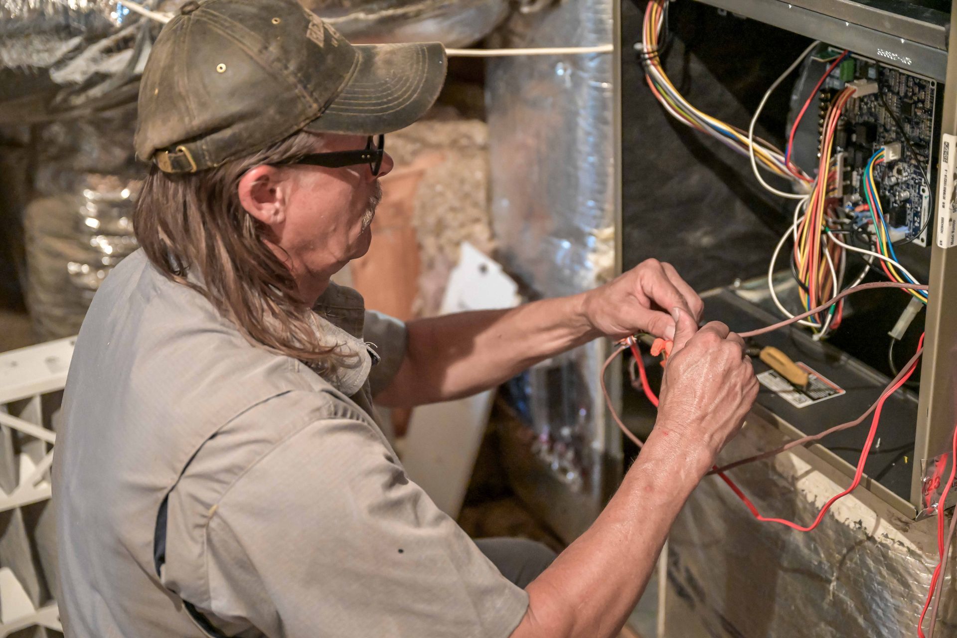 Person in cap and glasses, wiring a furnace.