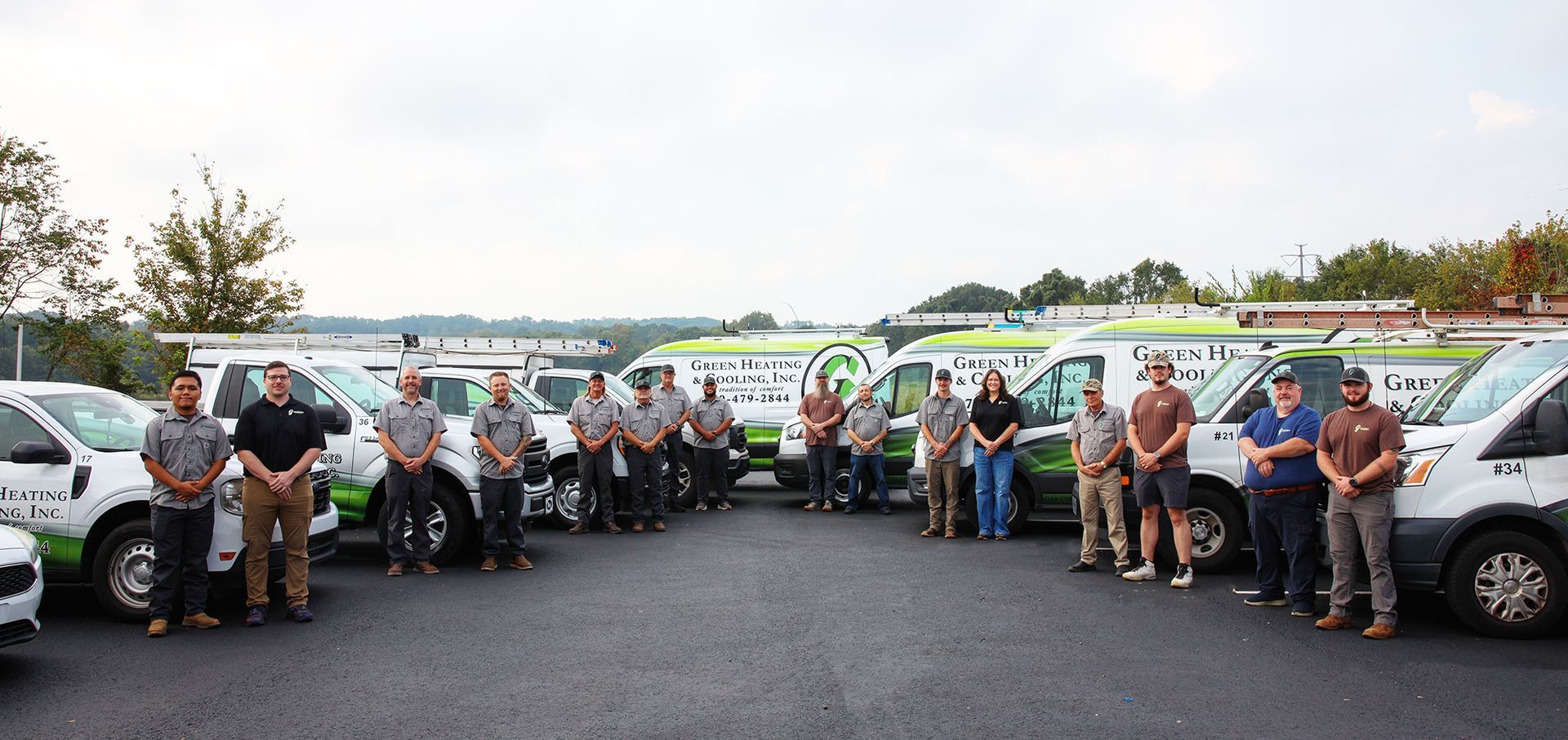 A group of people standing in front of several work vans in a parking lot. Cloudy sky in the background.