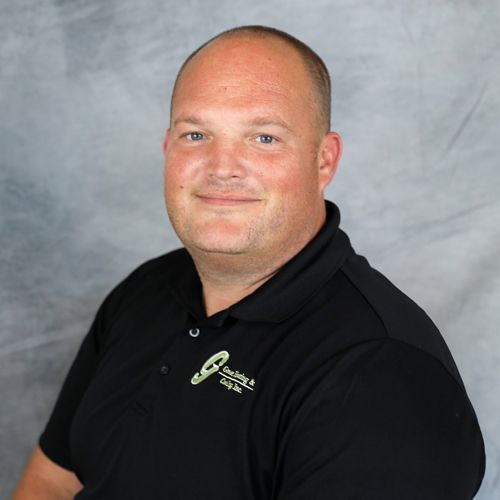 Man with short hair wearing a black polo shirt, smiling, in front of a gray backdrop.