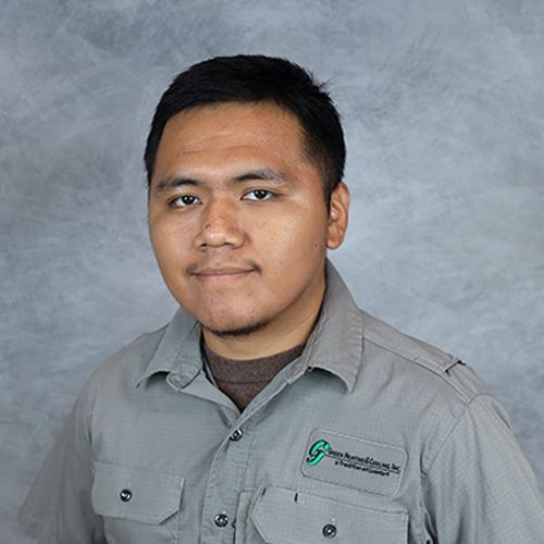 Man in grey work shirt, small goatee, looking directly at the viewer. Blurred, greyish background.