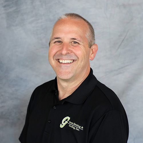 Man wearing a black polo shirt, smiling, with a logo on the shirt. Grey background.