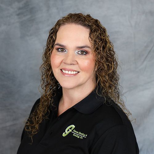 Woman with curly brown hair, wearing a black shirt with a company logo, smiling, and against a gray backdrop.