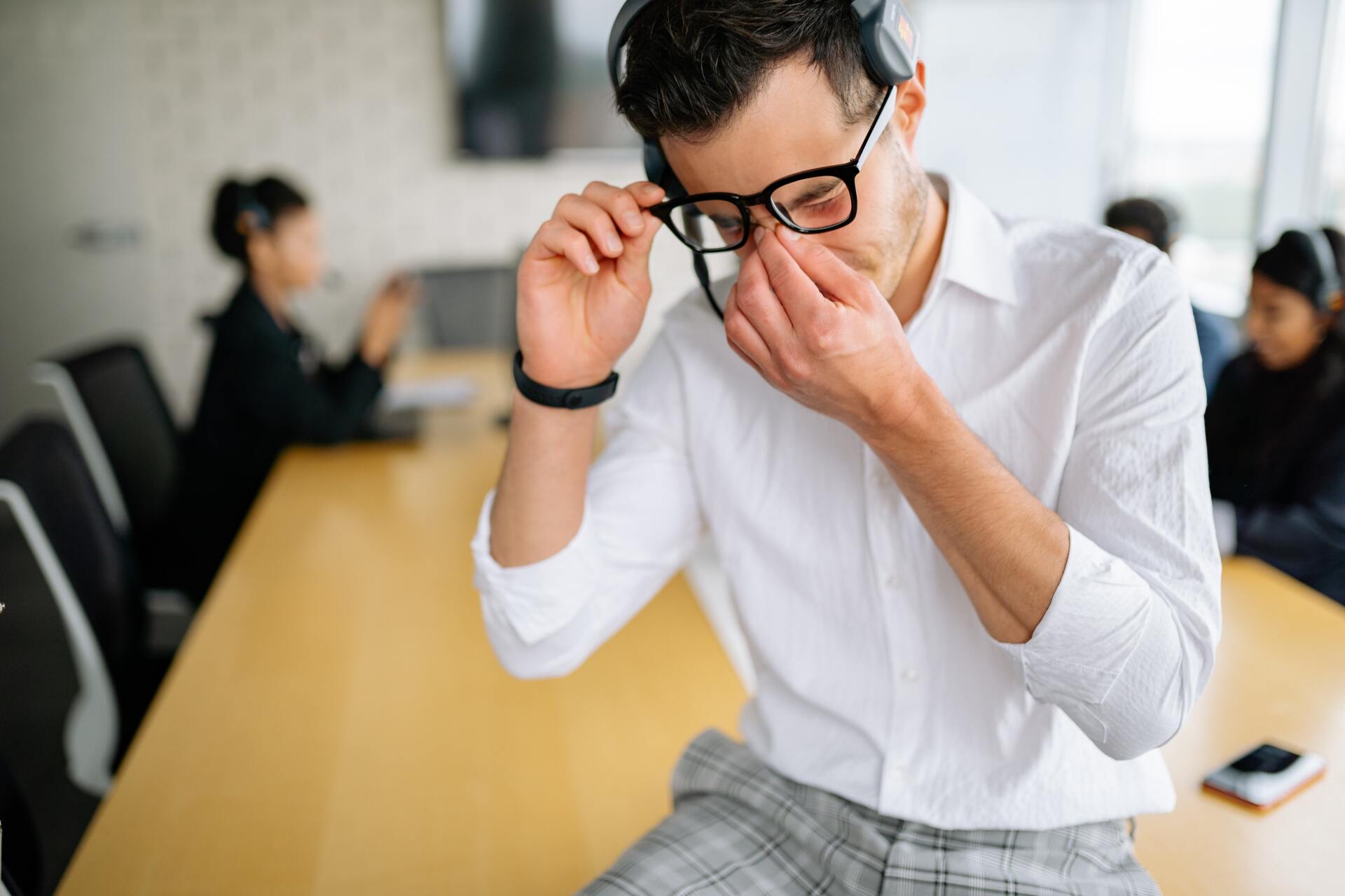 man scratching his eyes while sitting on a table