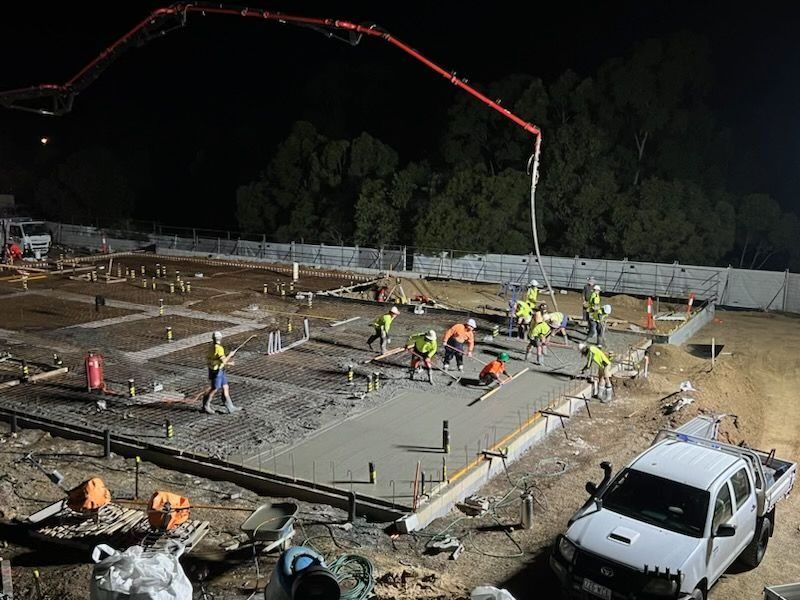 A Group Of Construction Workers Are Working On A Concrete Floor At Night — CQBB Concreting Pumping Pty Ltd In Barmaryee, QLD