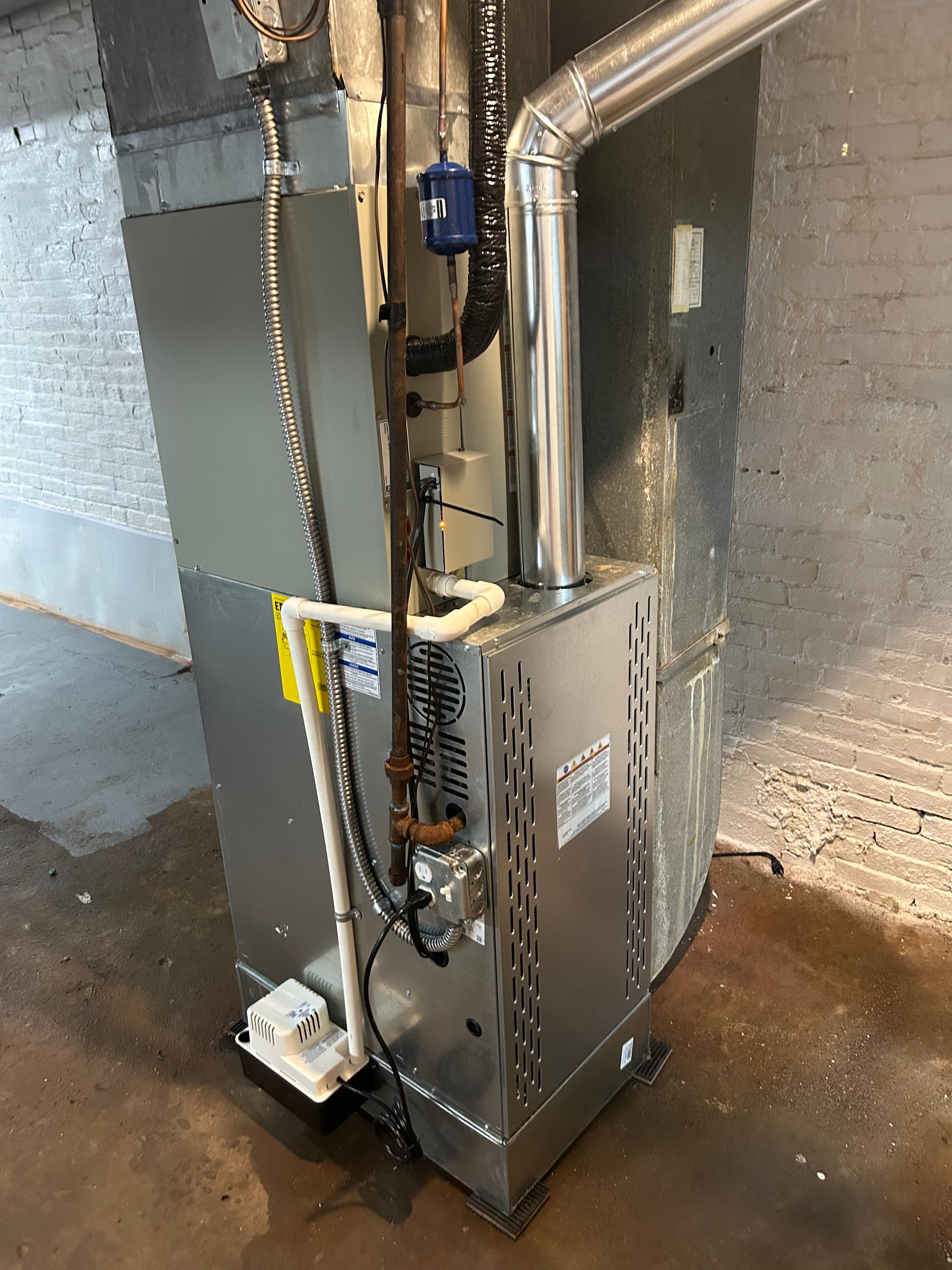 A new silver furnace installed in a concrete basement; pipes and ventilation are attached.