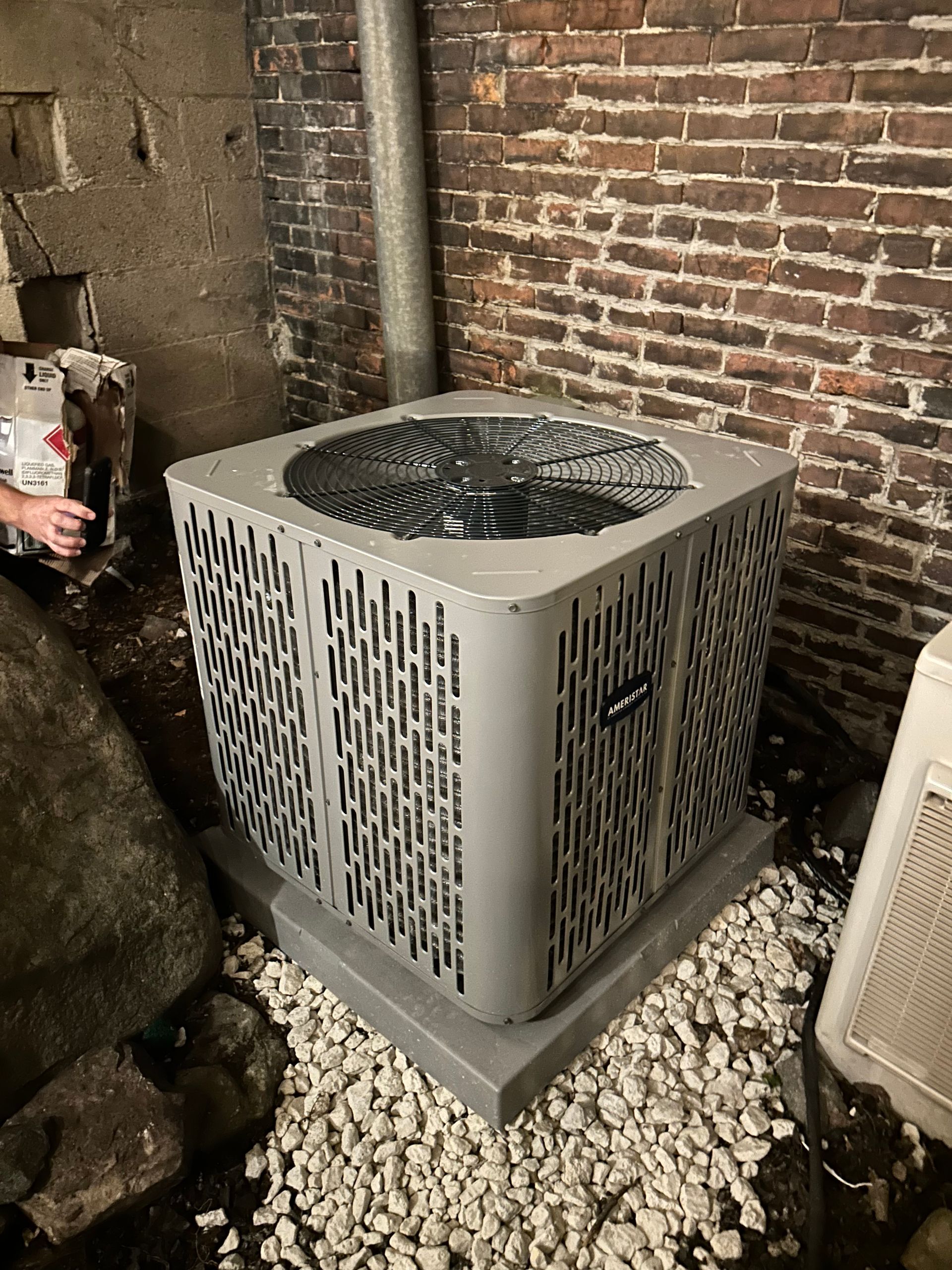 Air conditioning unit on a concrete base in a basement with brick walls.