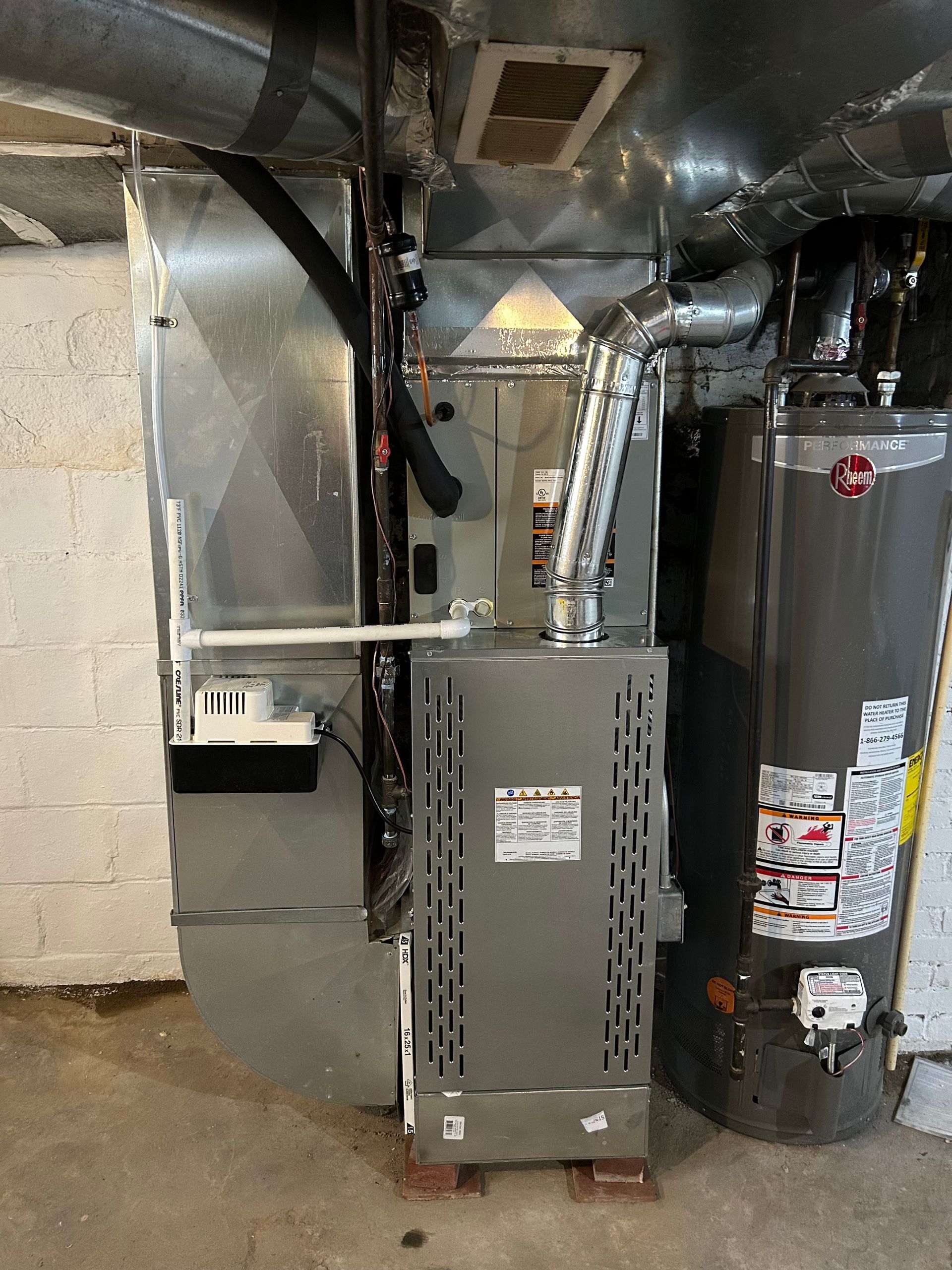 A furnace and water heater in a basement. Gray metal units and ductwork.