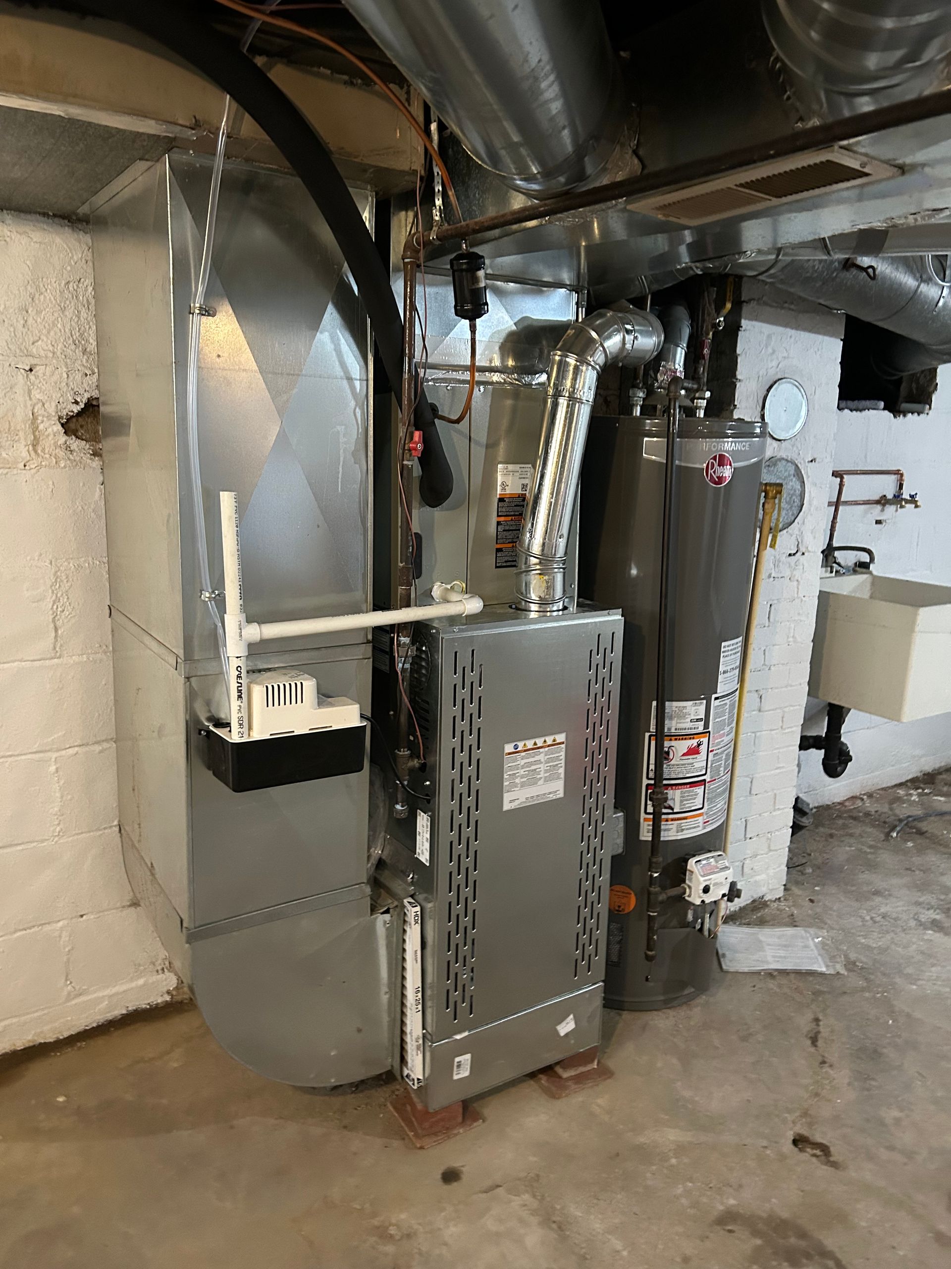 Furnace and water heater in a basement; silver, gray appliances against white and concrete walls.