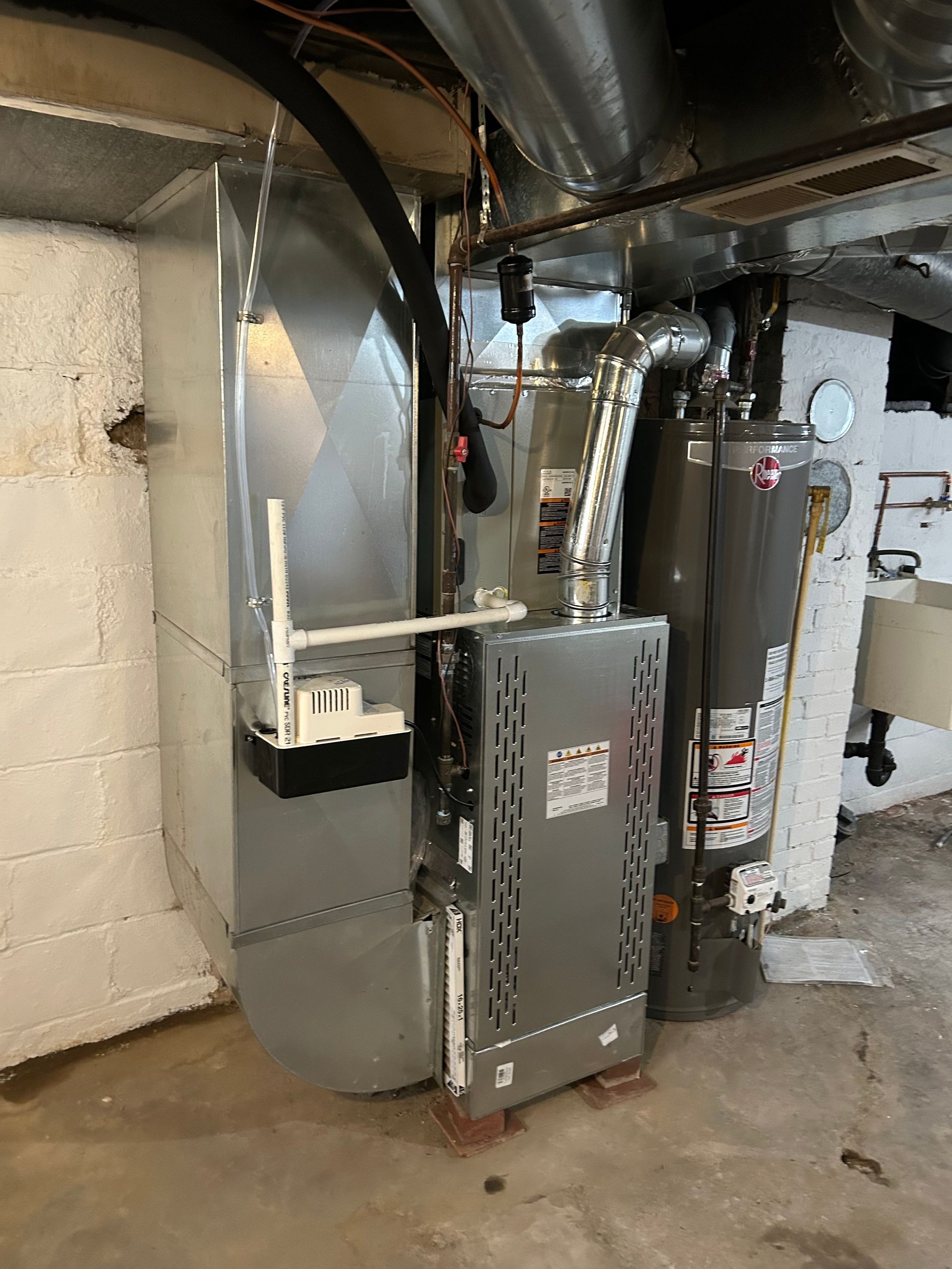 Furnace, ductwork, and water heater in a basement with white walls and concrete floor.
