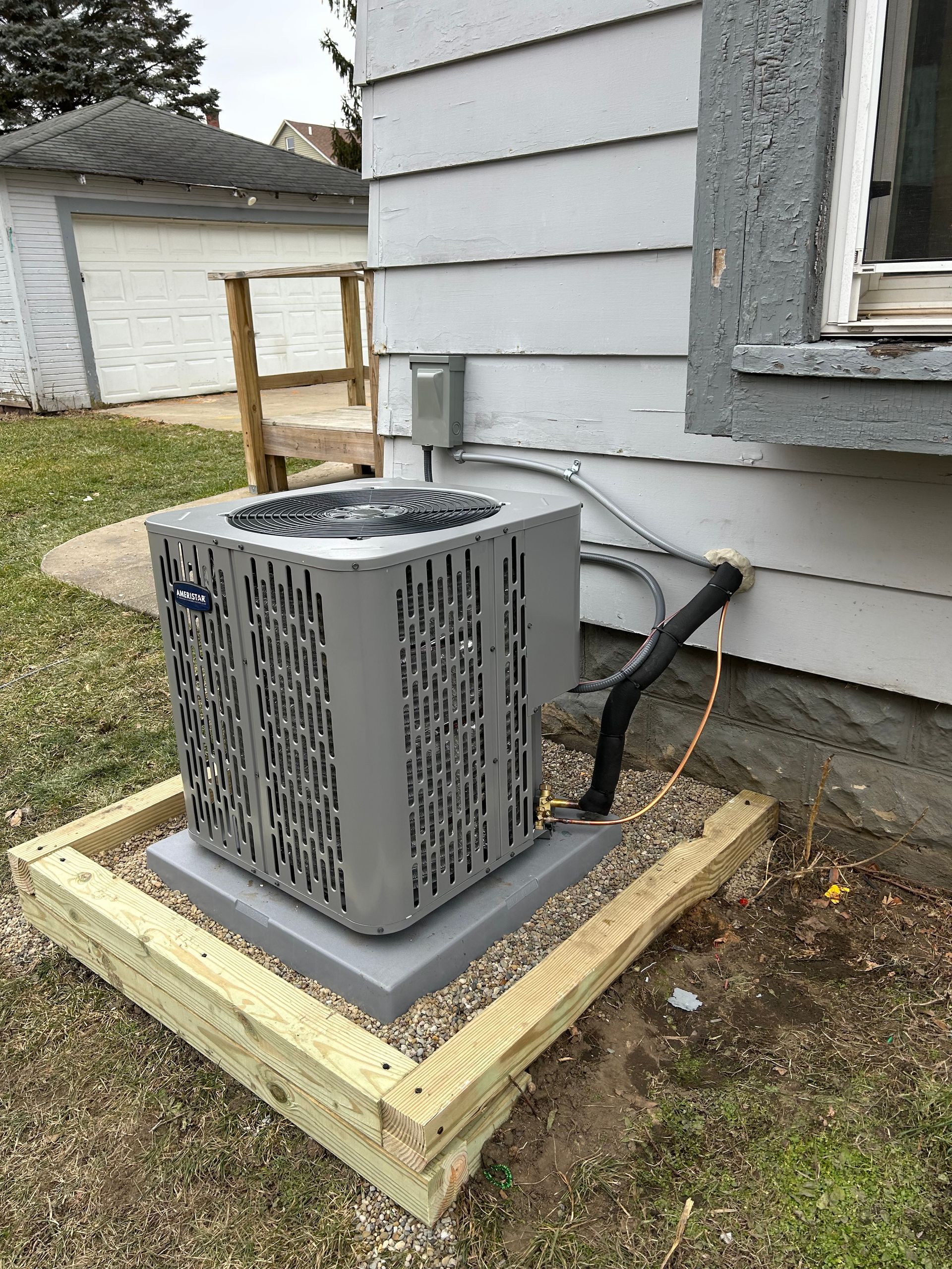 Air conditioning unit outside a house on a concrete pad within a wooden frame.