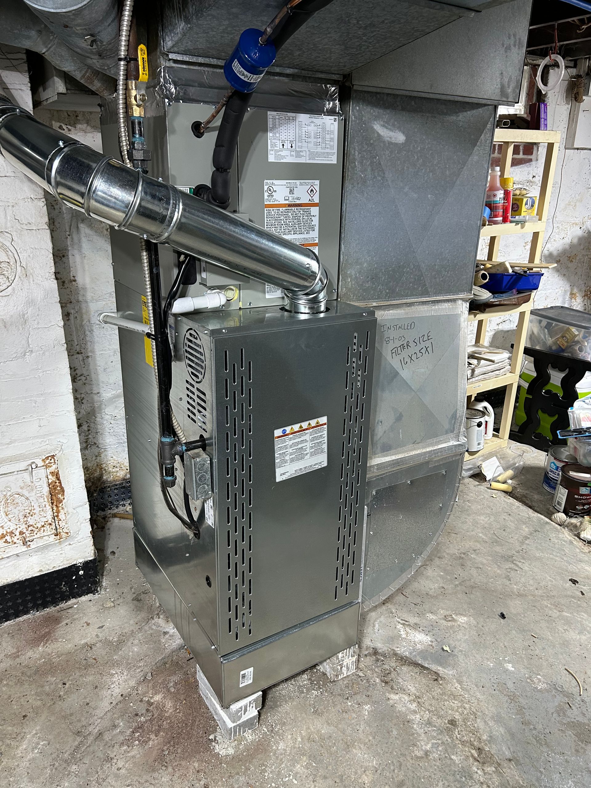 A gas furnace, silver and gray, sits on concrete floor in basement with ductwork and pipes.