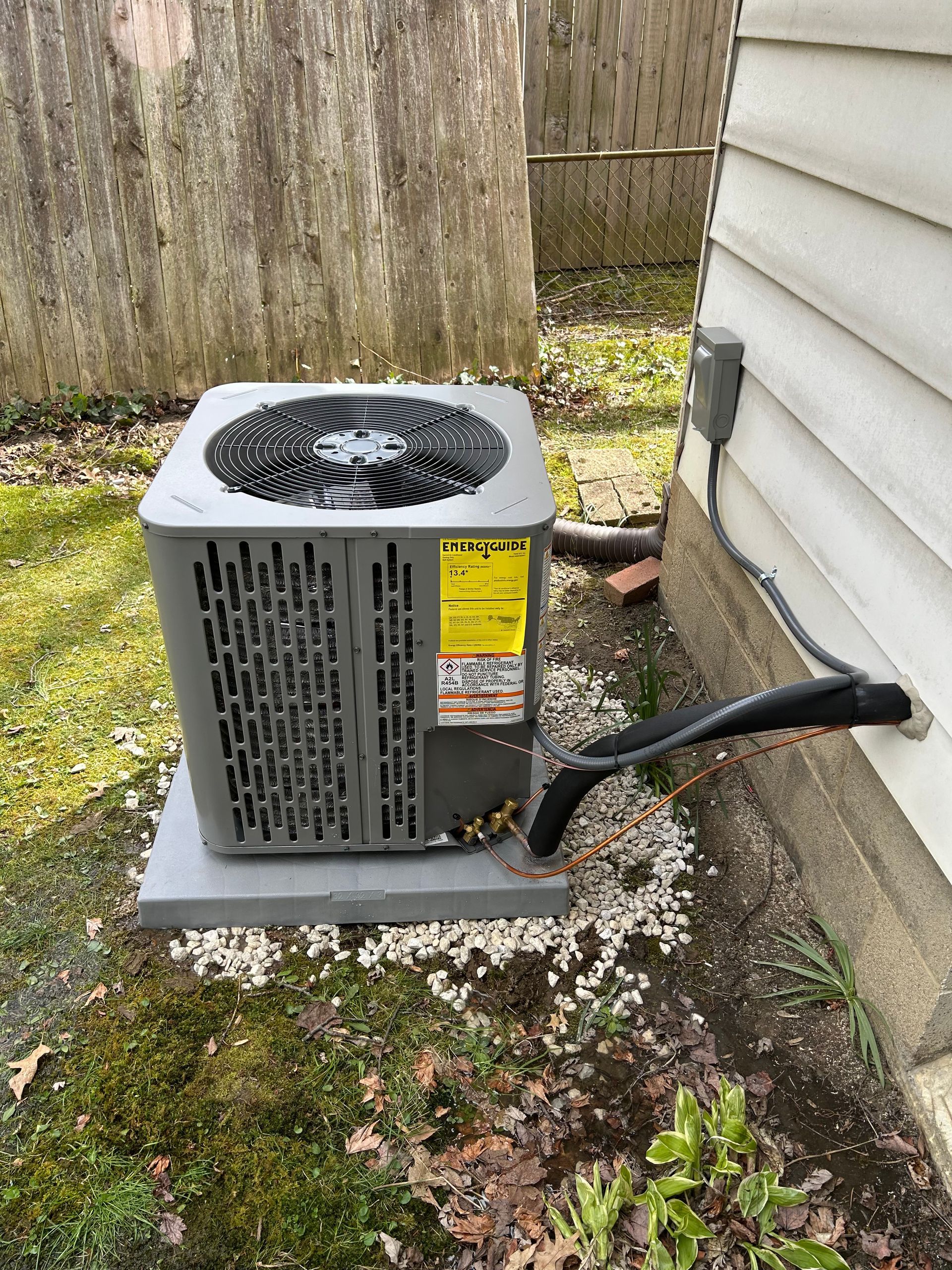 Air conditioning unit on a concrete pad next to a house. Green grass and white gravel surround it.