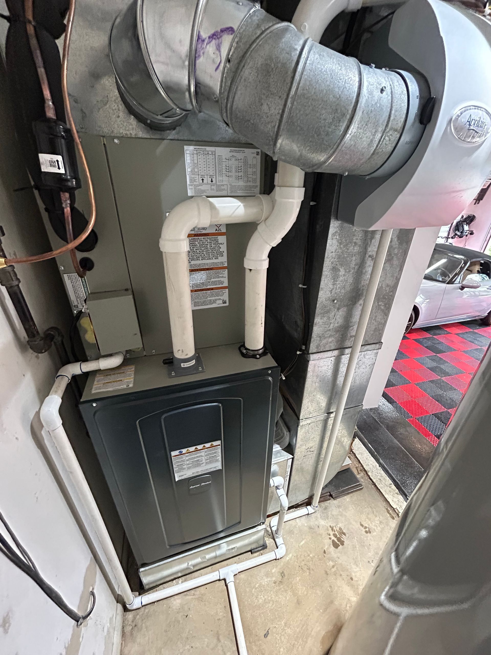 Furnace and air ducts in a utility room, with white PVC pipes.