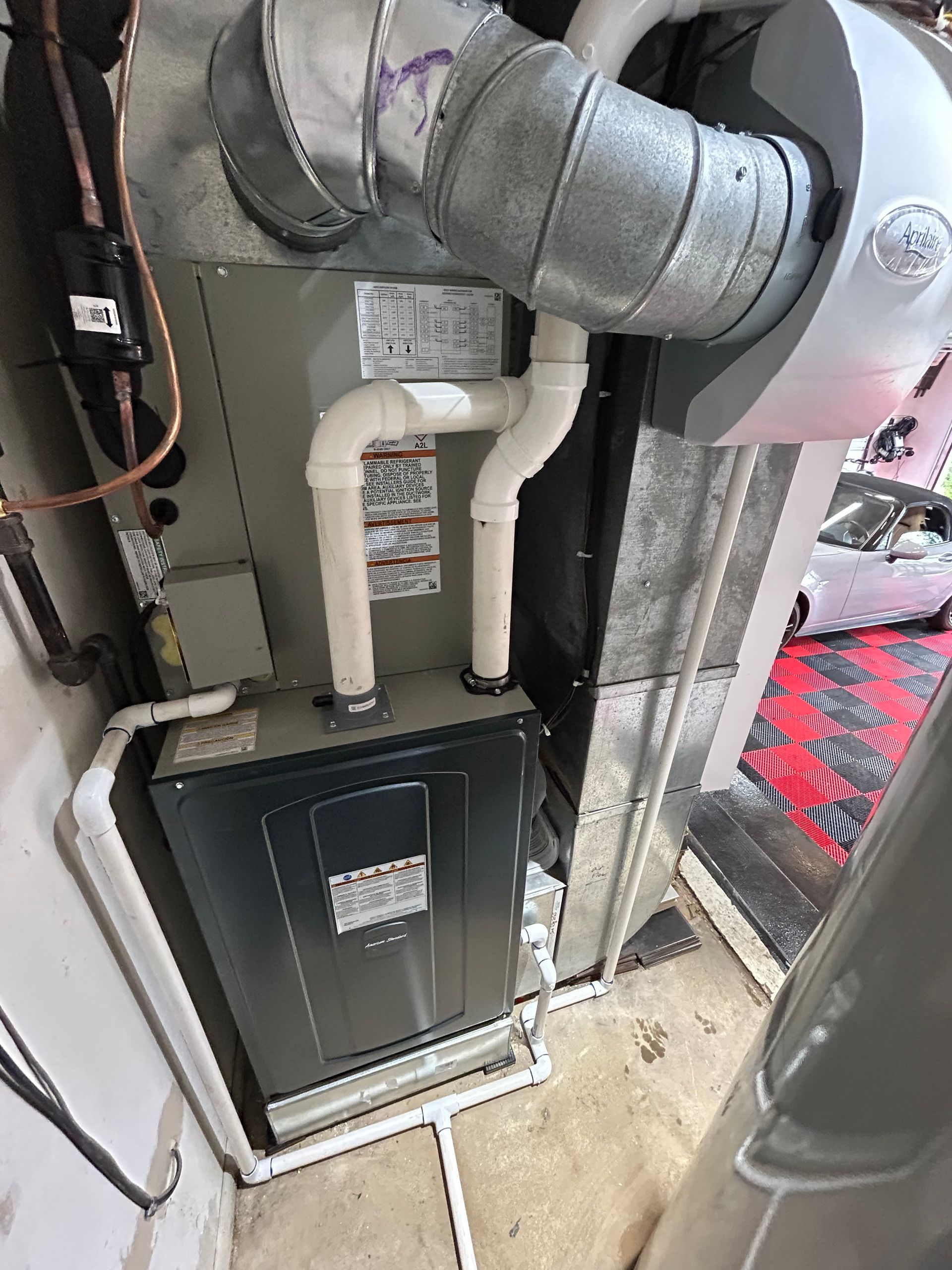 HVAC unit with metal ductwork and white PVC pipes in a utility room.
