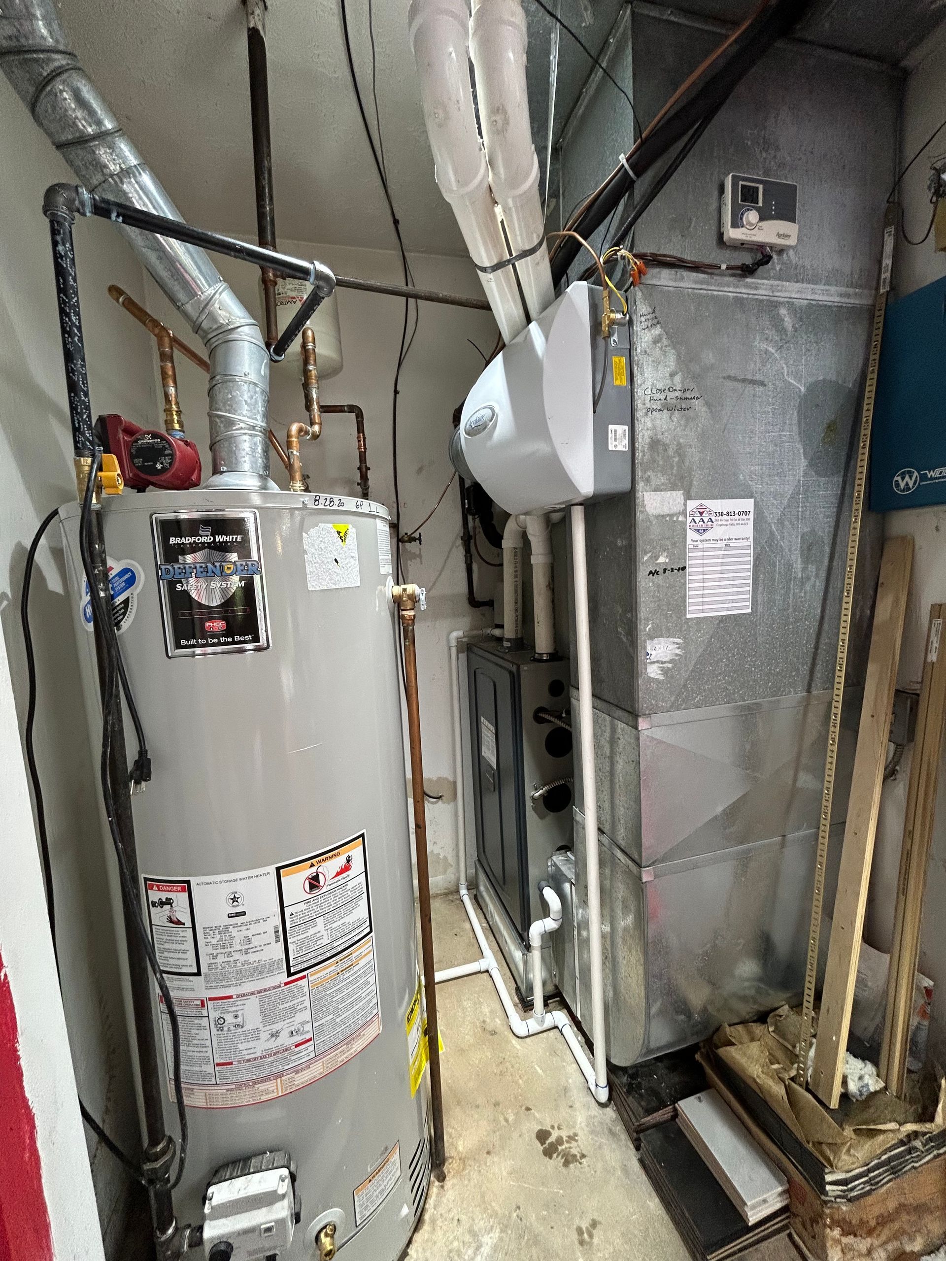 Water heater and furnace in an indoor utility room, with ductwork and pipes.
