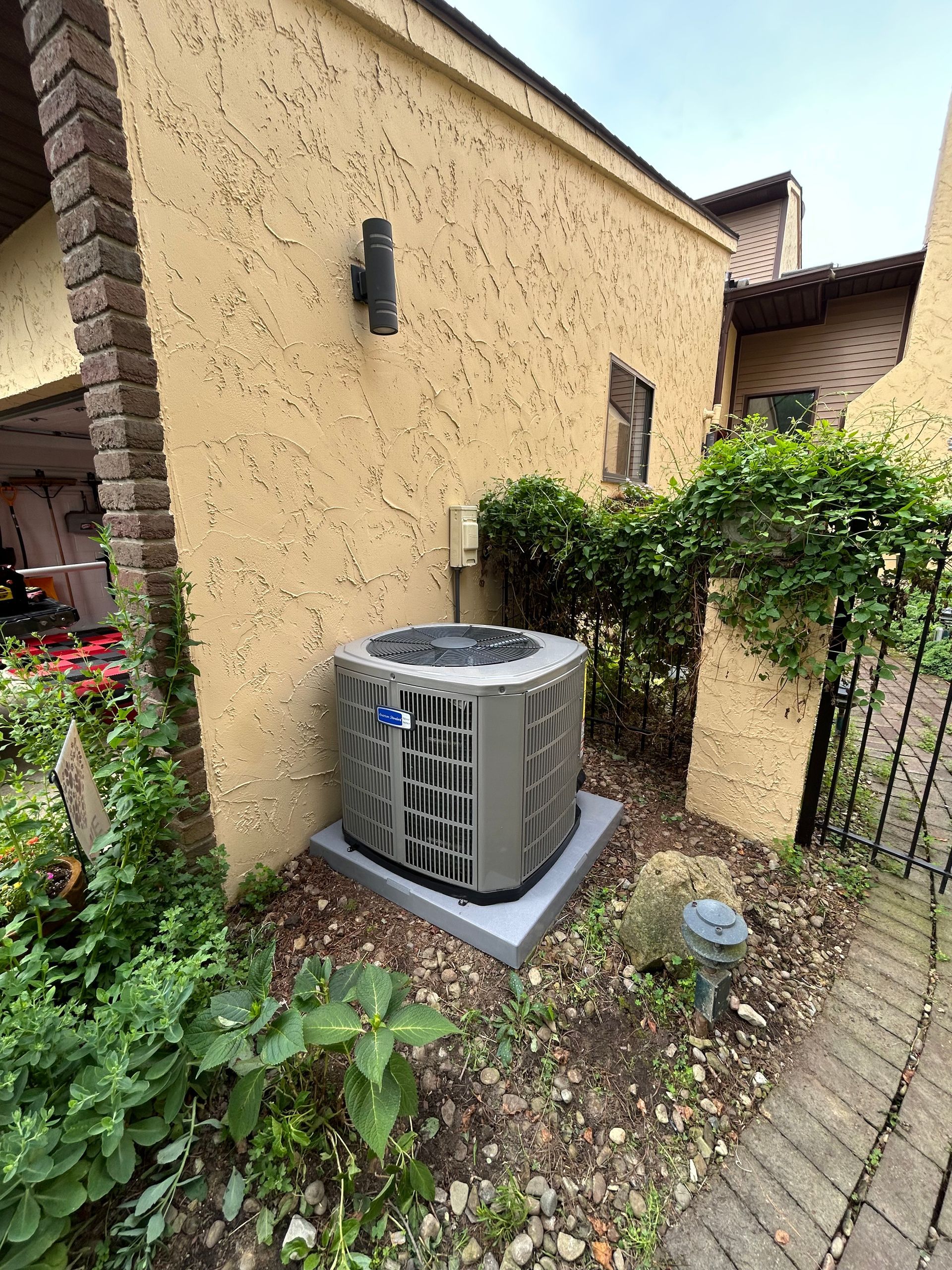 Air conditioner unit on a concrete base next to a beige building with landscaping.