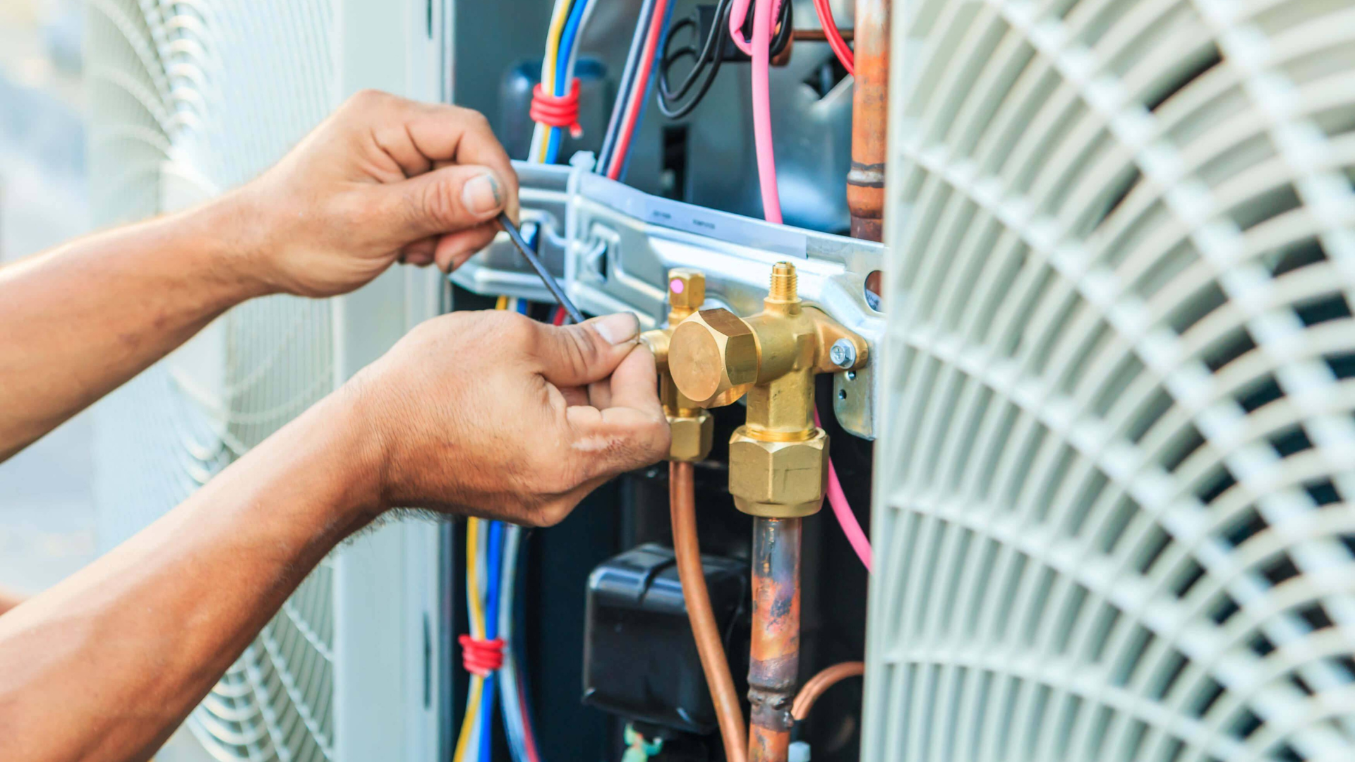 Hands of a technician working on an air conditioning unit's copper tubing.
