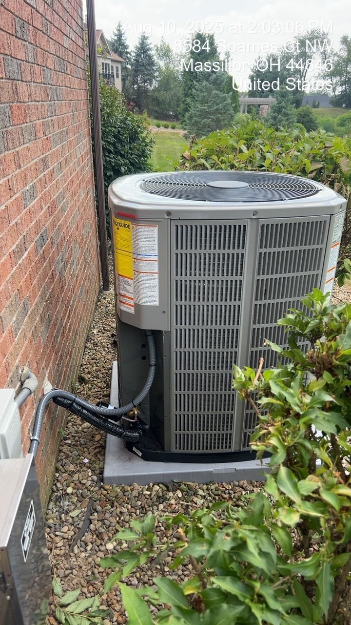 AC unit next to a brick wall and bushes. Gray unit, surrounded by landscaping.